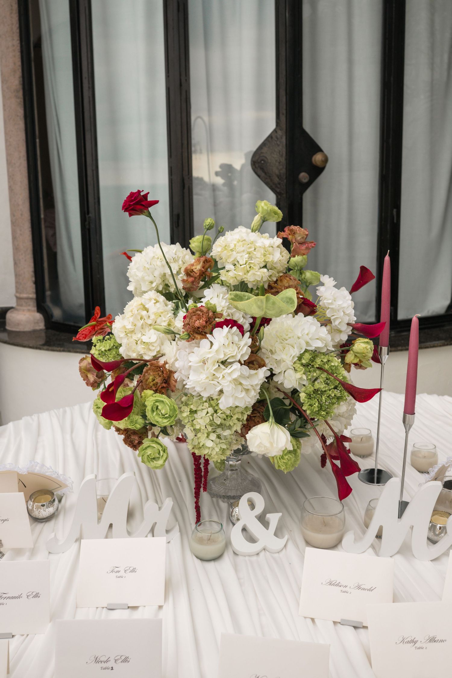 Elegant wedding head table with white and red floral centerpiece, Mr & Mrs signs, and red taper candles.