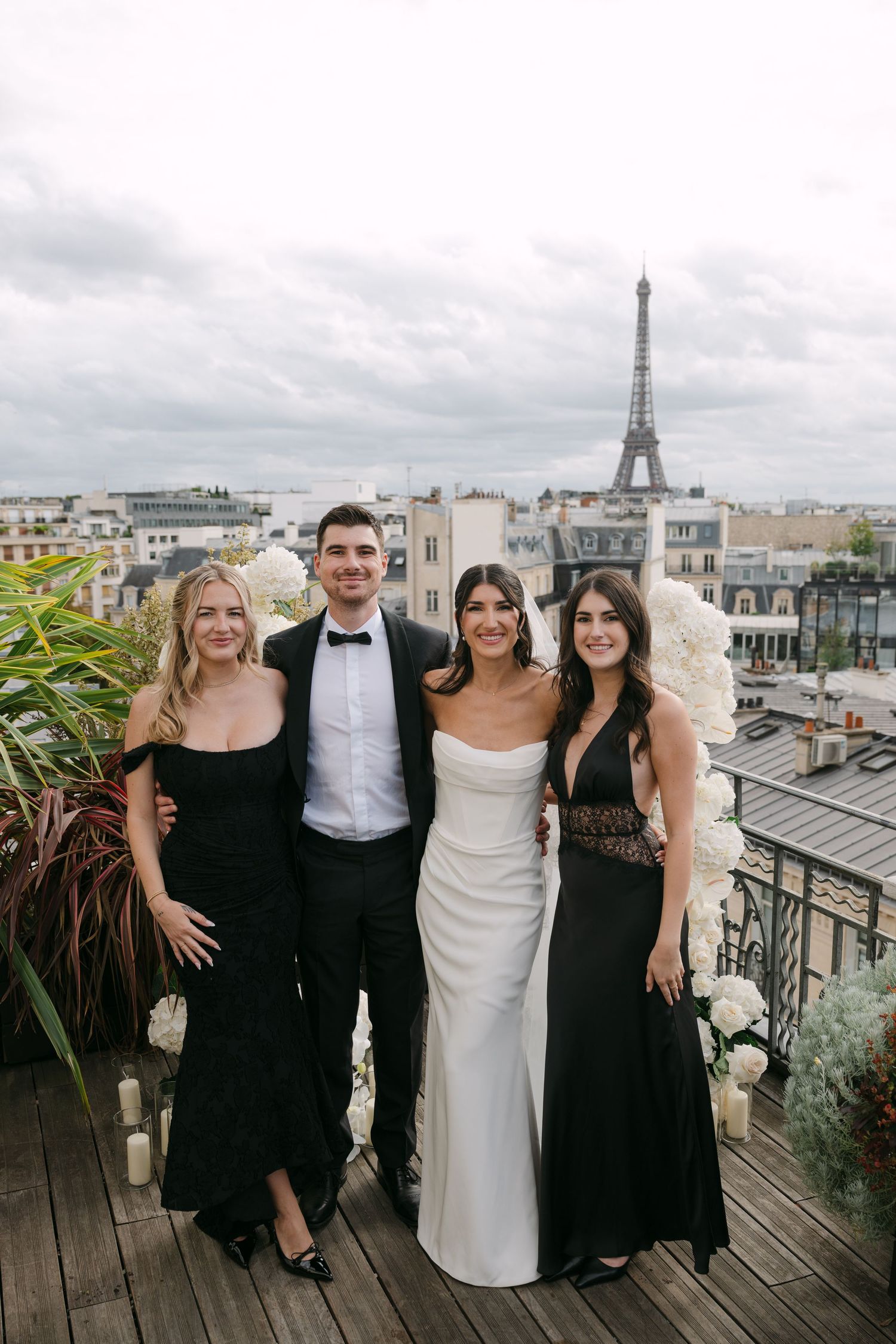 Bride posing with wedding guests in formal black attire on a Paris rooftop with the Eiffel Tower behind them.