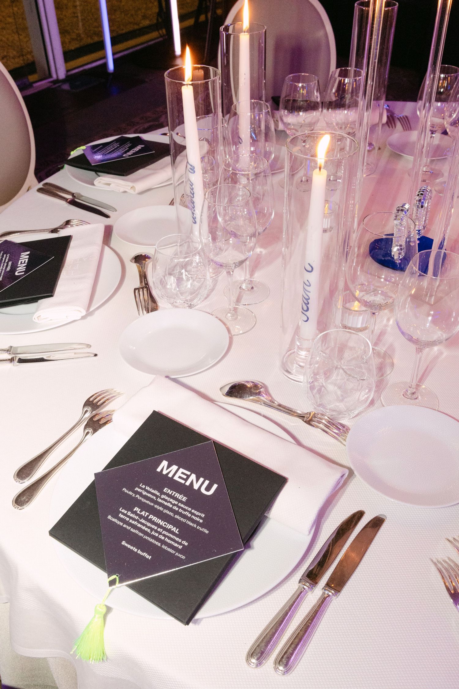 Formal wedding dinner table setting with black menu cards, candles, crystal glasses, and silverware.
