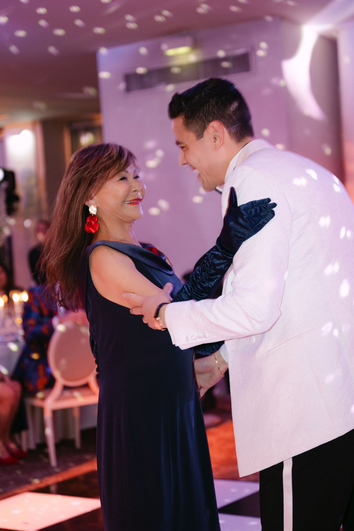 Mother and son share a joyful dance at wedding reception under sparkling disco ball lights.