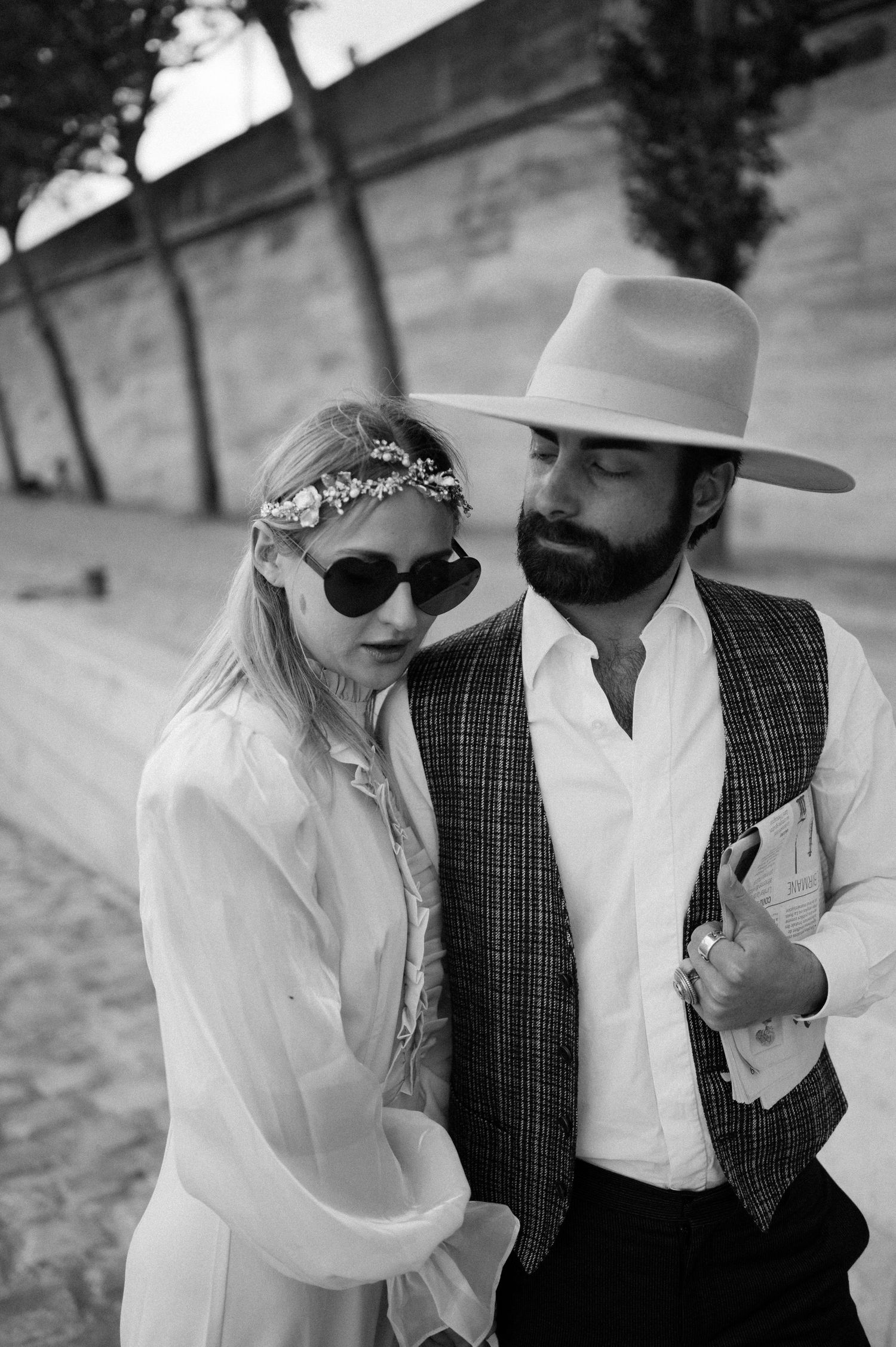 A romantic black and white portrait of a couple in vintage attire near a stone wall.