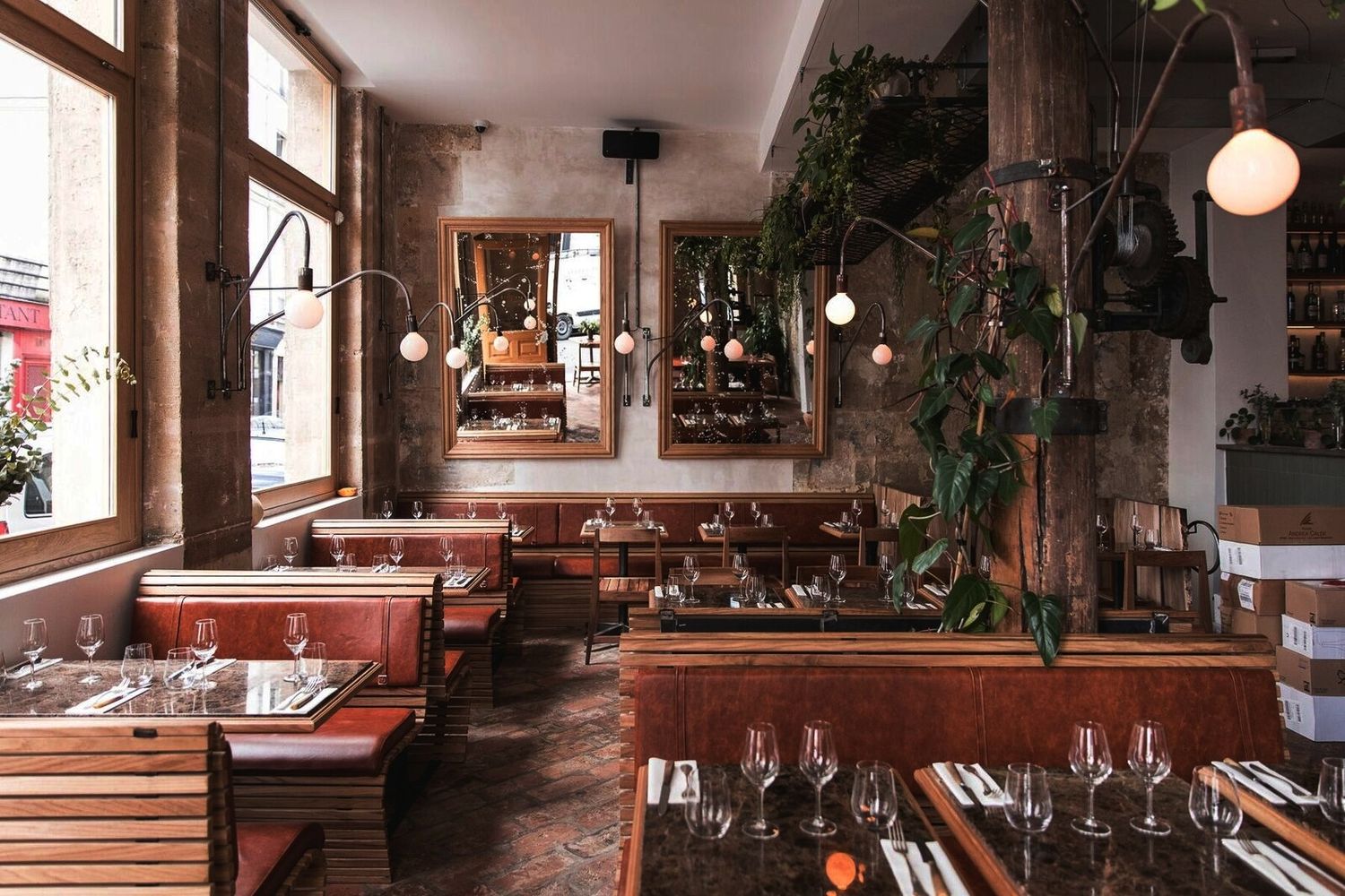 Rustic restaurant interior with wooden tables, wine glasses, and hanging plants creating an intimate atmosphere.