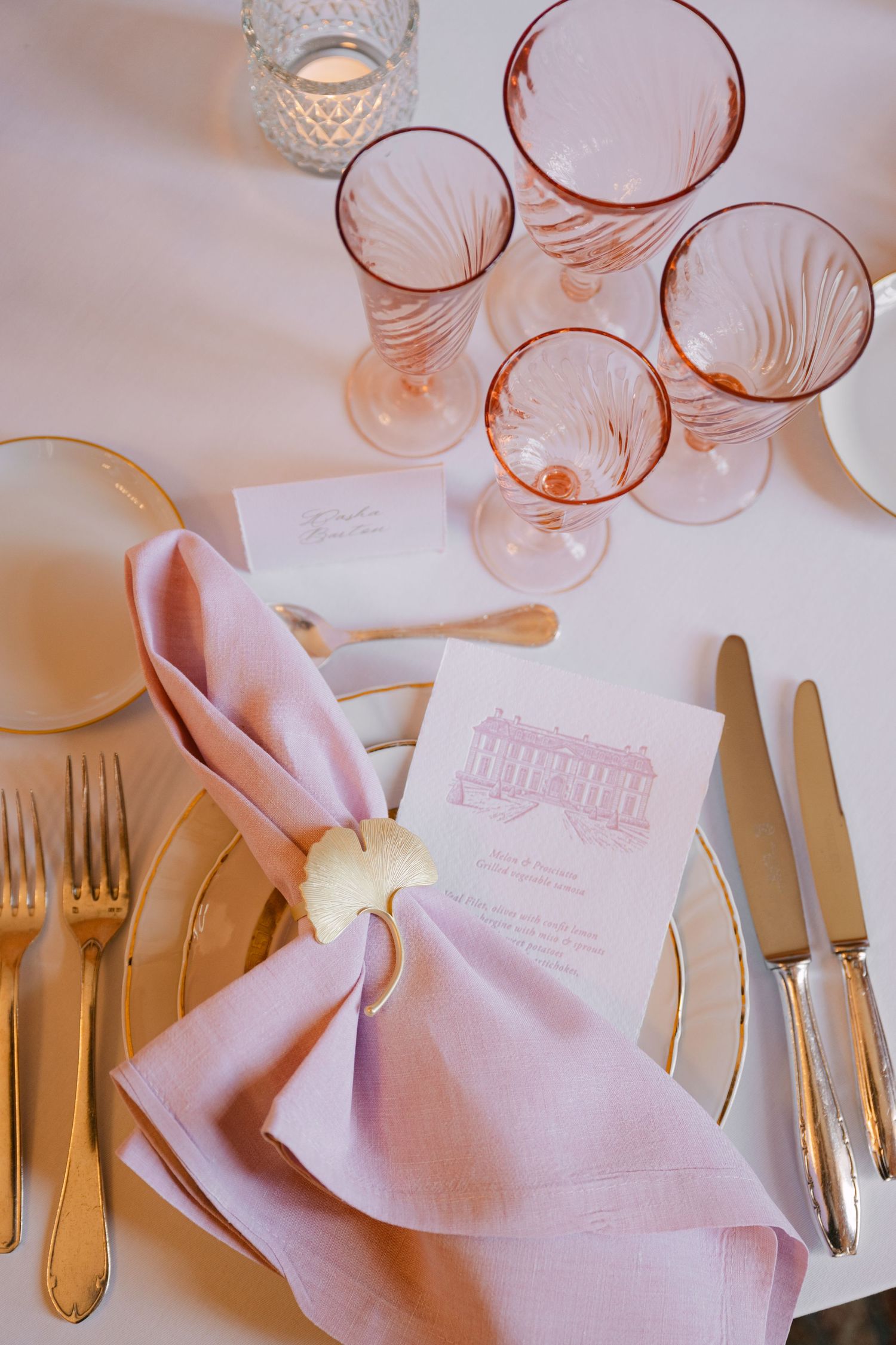 Elegant wedding place setting with pink linen napkin, gold butterfly ring, pink menu card, and rose-tinted glassware.
