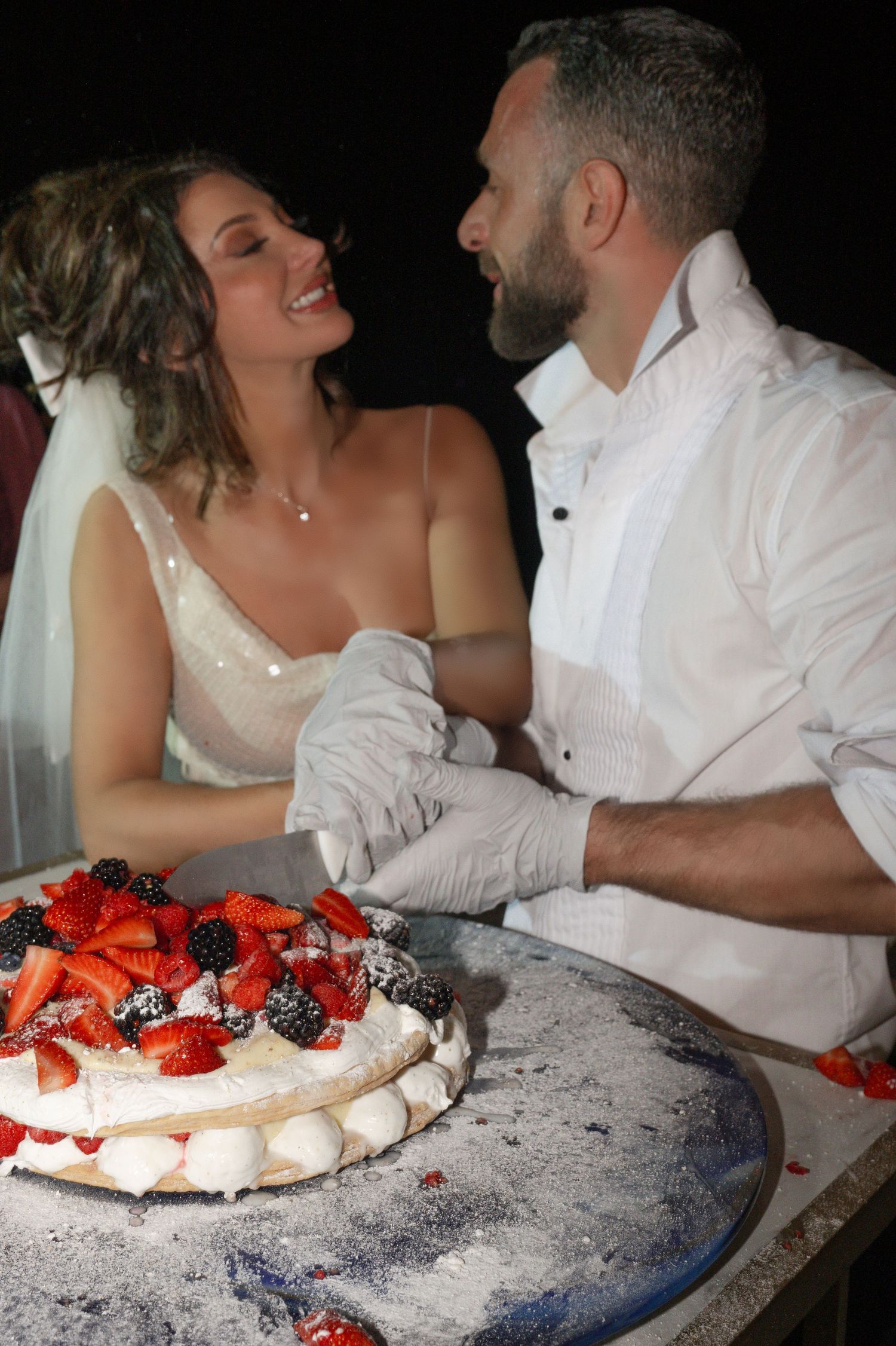 Smiling bride and groom cutting fruit wedding cake together.