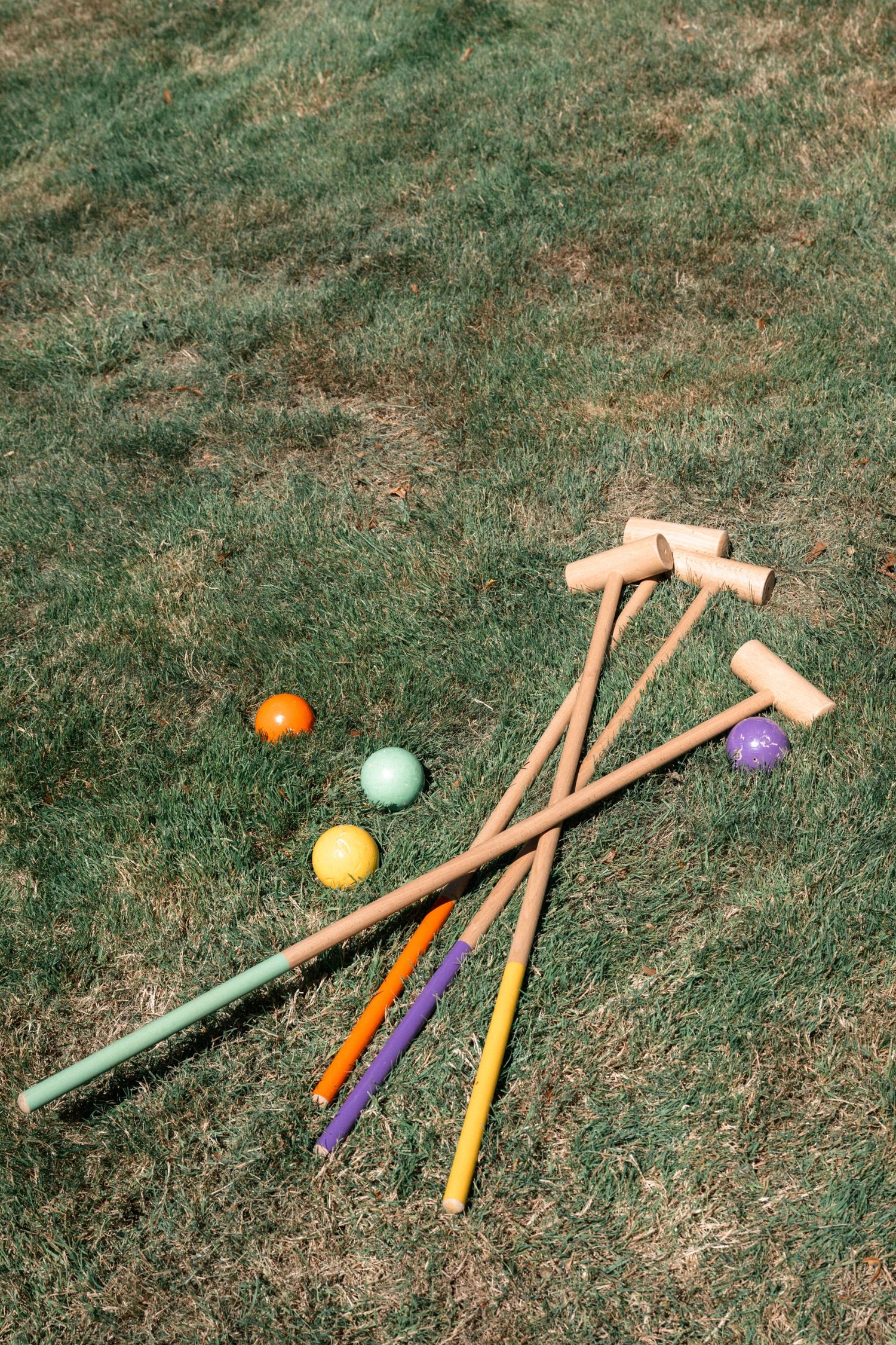 Colorful croquet mallets and balls scattered on green grass for an outdoor lawn game at a garden party.