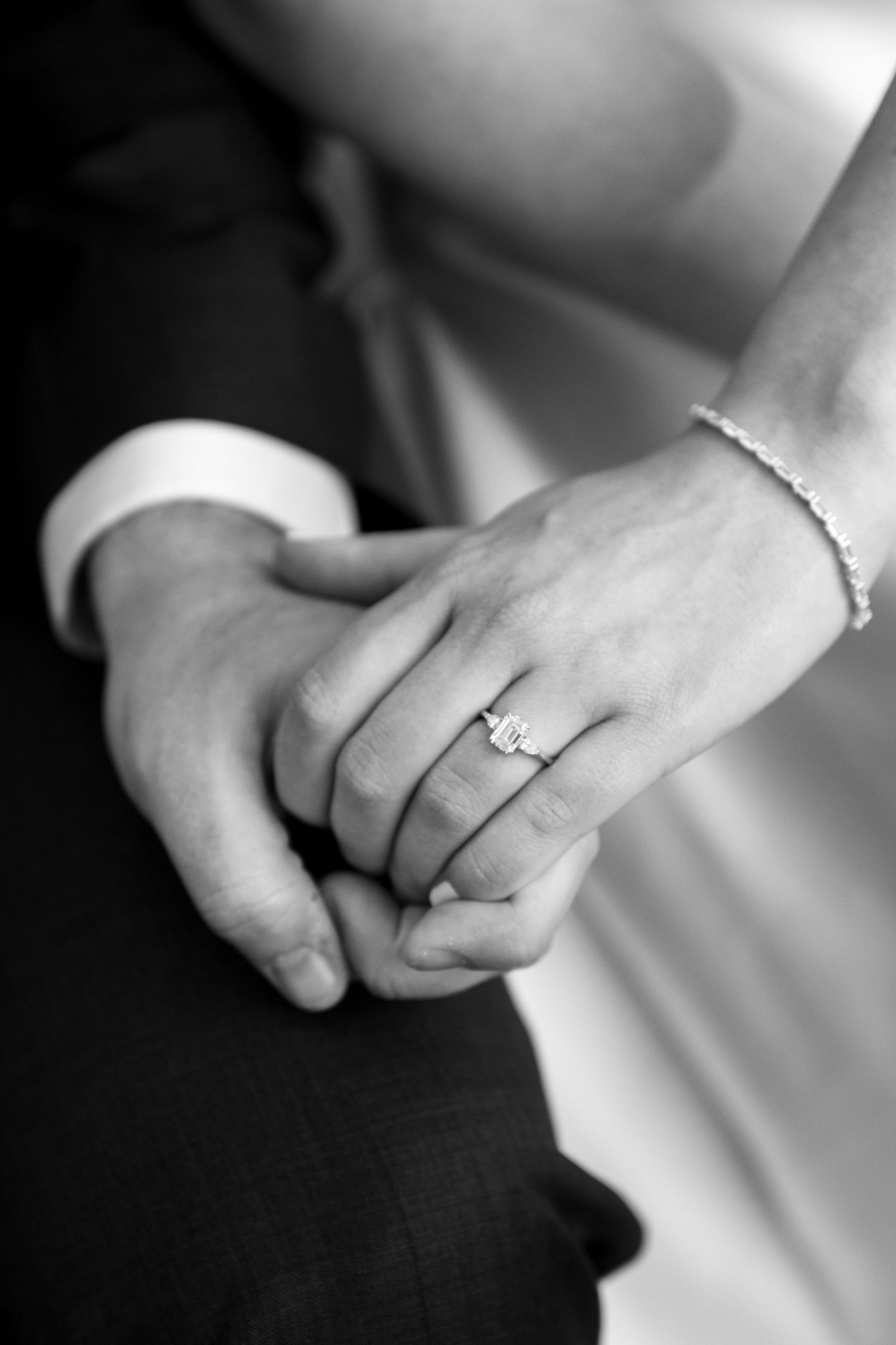 Black and white close-up of bride and groom holding hands showing elegant emerald cut engagement ring.