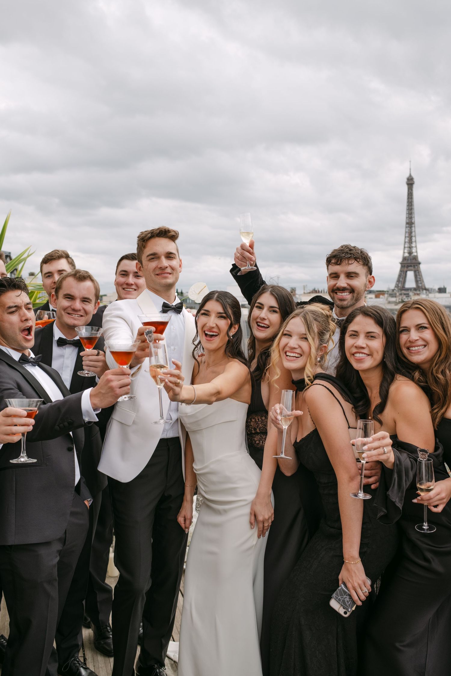 Bride and groom celebrating with wedding guests holding champagne on a Paris rooftop with Eiffel Tower backdrop.