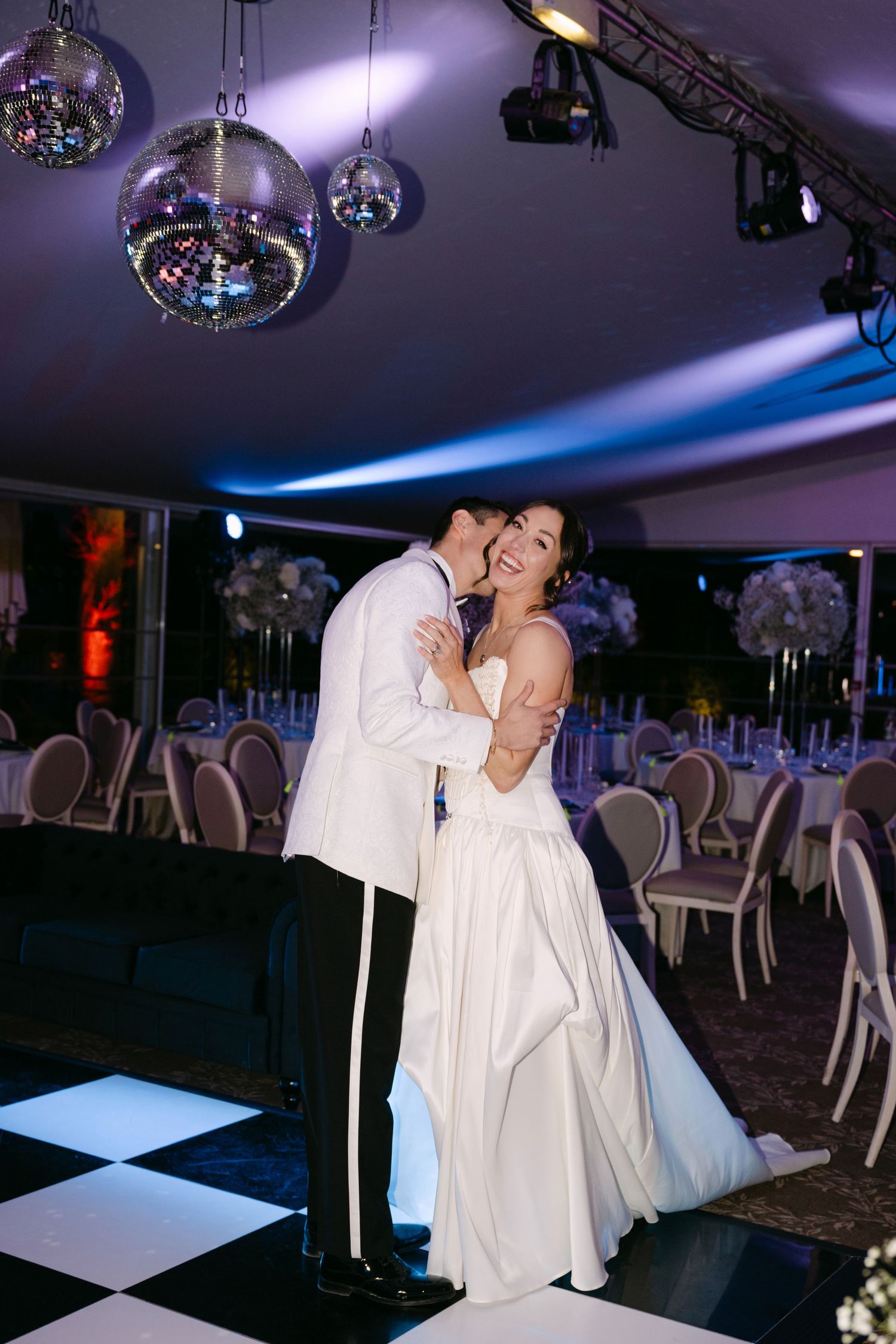 Bride and groom sharing romantic first dance under disco balls on checkered dance floor at wedding.