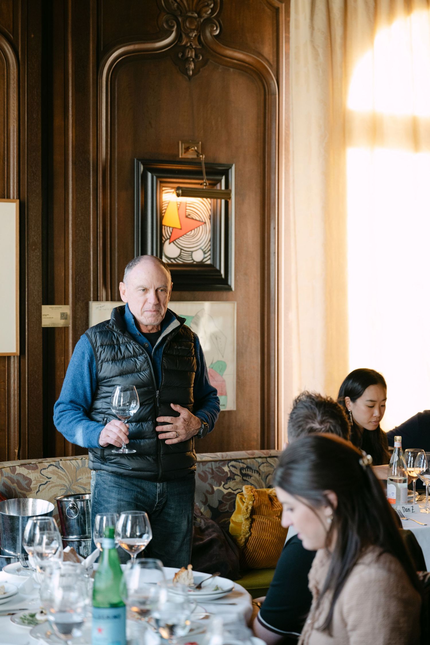 Man holding wine glass standing in ornate wood-paneled fine dining restaurant.