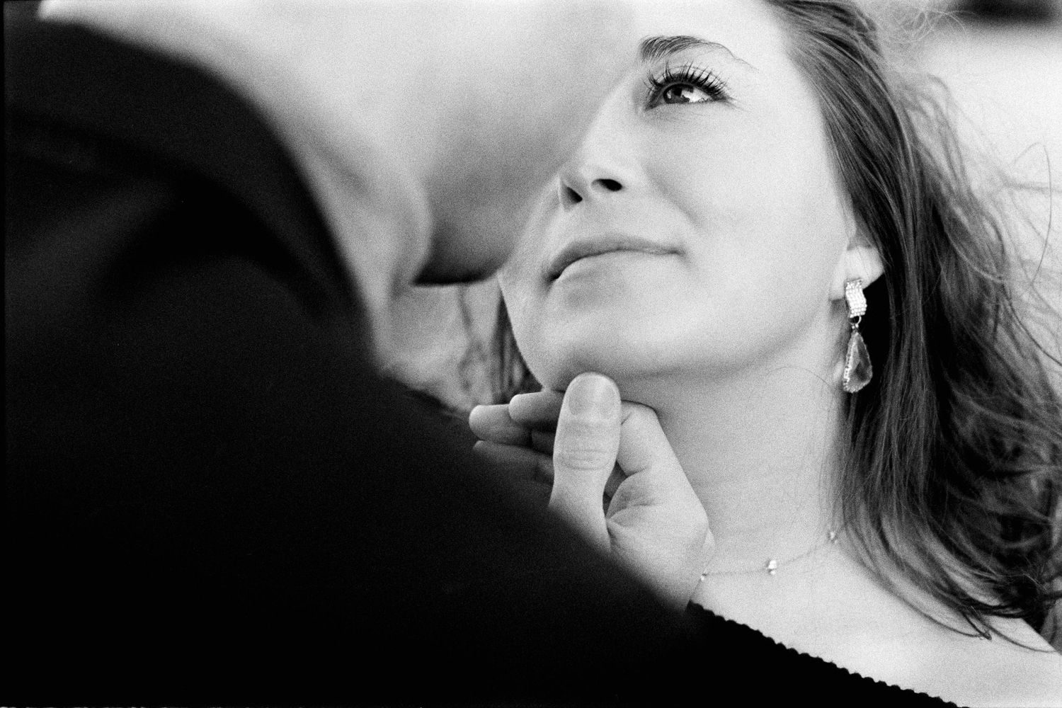 Black and white close-up of a man tenderly lifting a smiling woman's chin in an intimate moment.