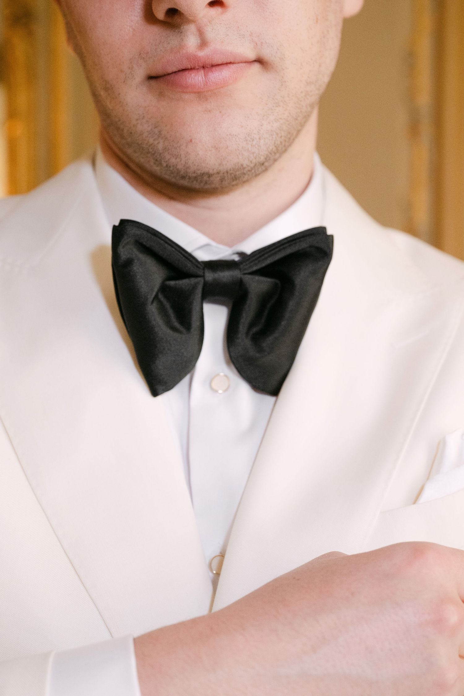 Close-up of groom in white tuxedo jacket wearing a large black satin bow tie on wedding day.
