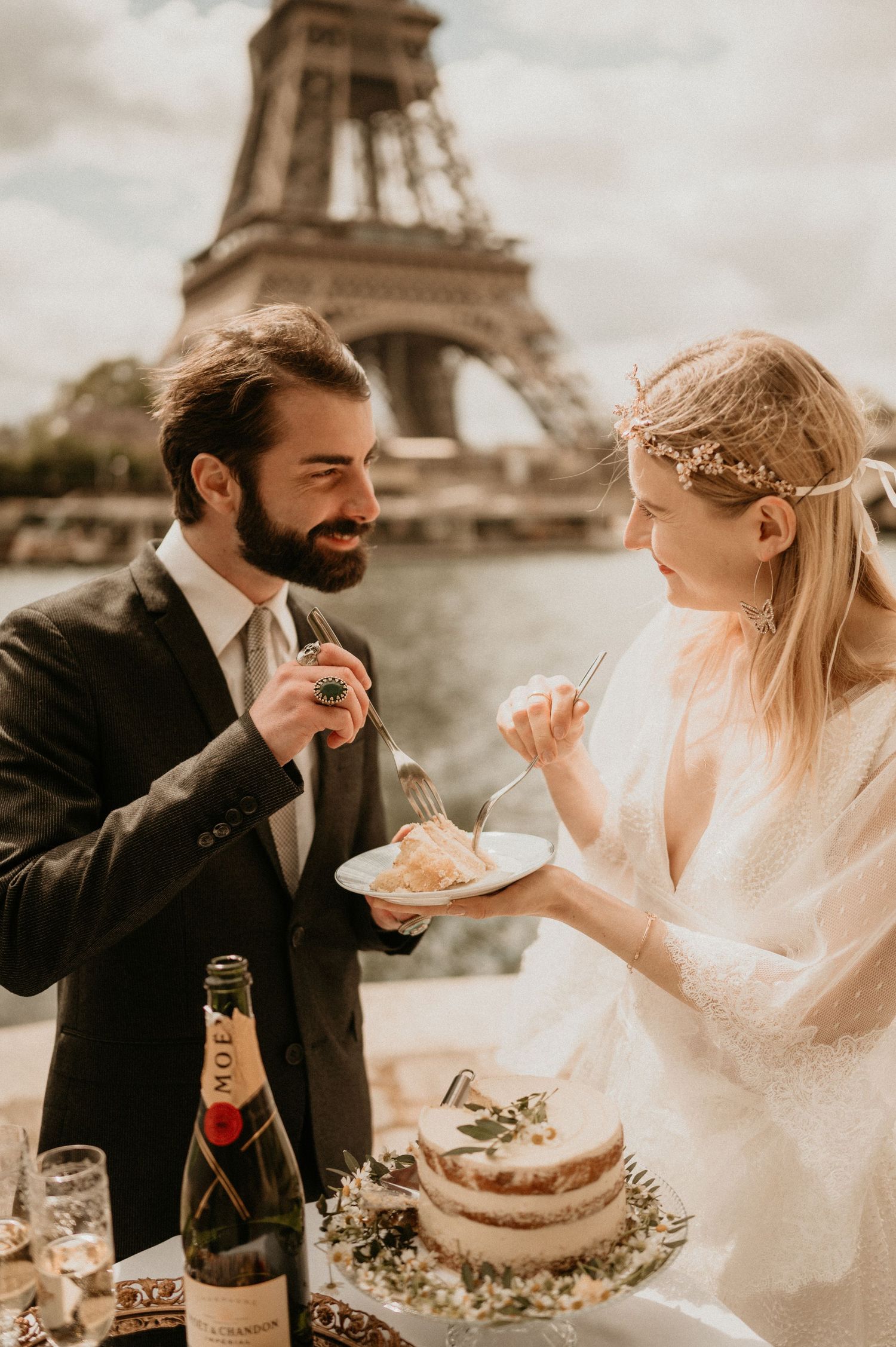 A joyful newlywed couple sharing cake with the Eiffel Tower as their backdrop.