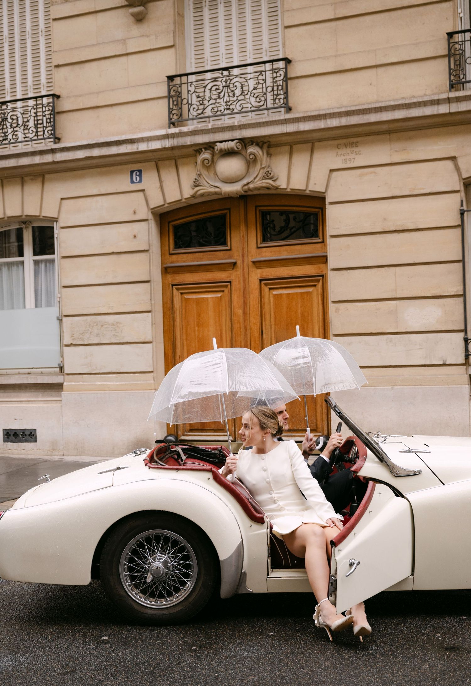 White vintage sports car with flowing veil draped along its side on a cobblestone street.
