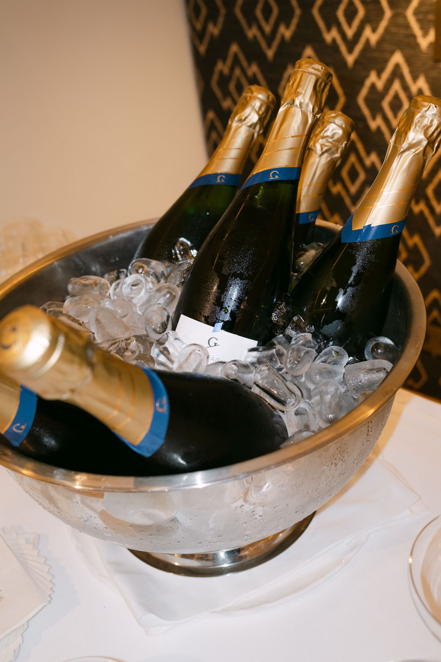 Champagne bottles chilling in ice buckets against a patterned wallpaper background.