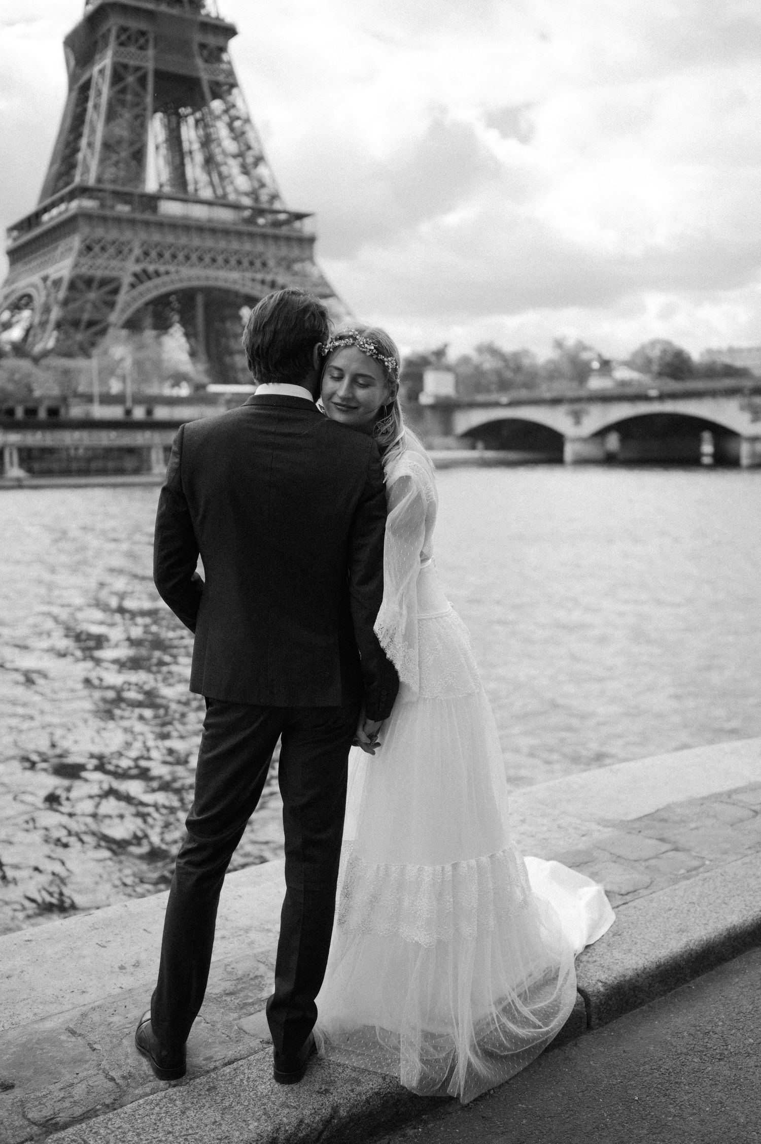 Black and white wedding photograph of a couple by the Eiffel Tower along the Seine River.