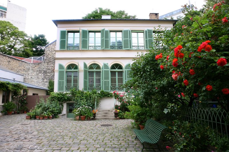 Elegant green Parisian house with arched windows and blooming red roses in the garden.