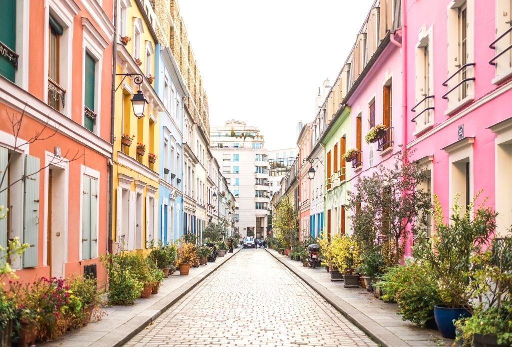 Colorful row of pastel painted houses on a cobblestone street in Paris with potted plants.