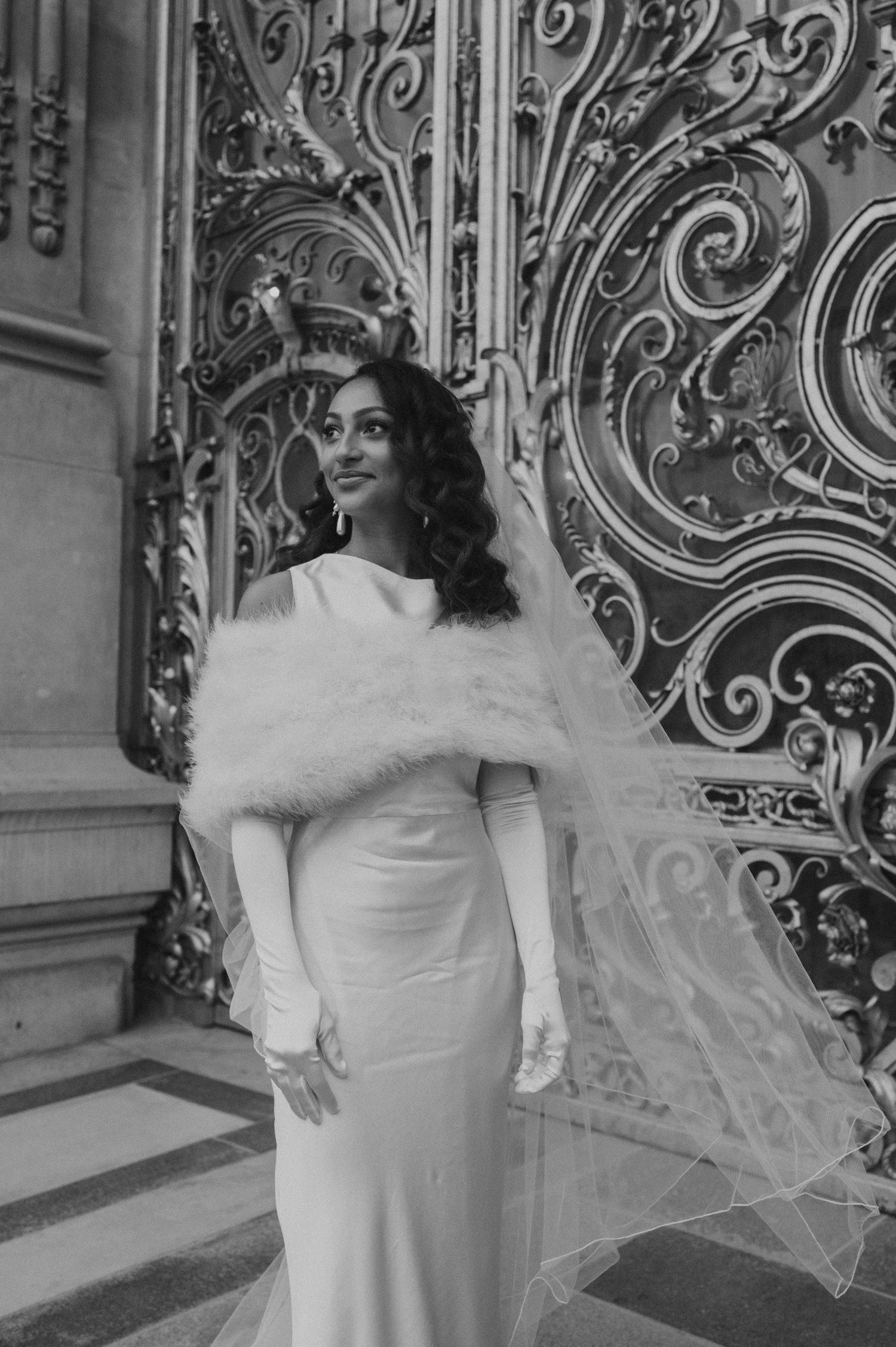 Elegant bridal portrait showcasing a white dress and fur stole against ornate decorative gates.