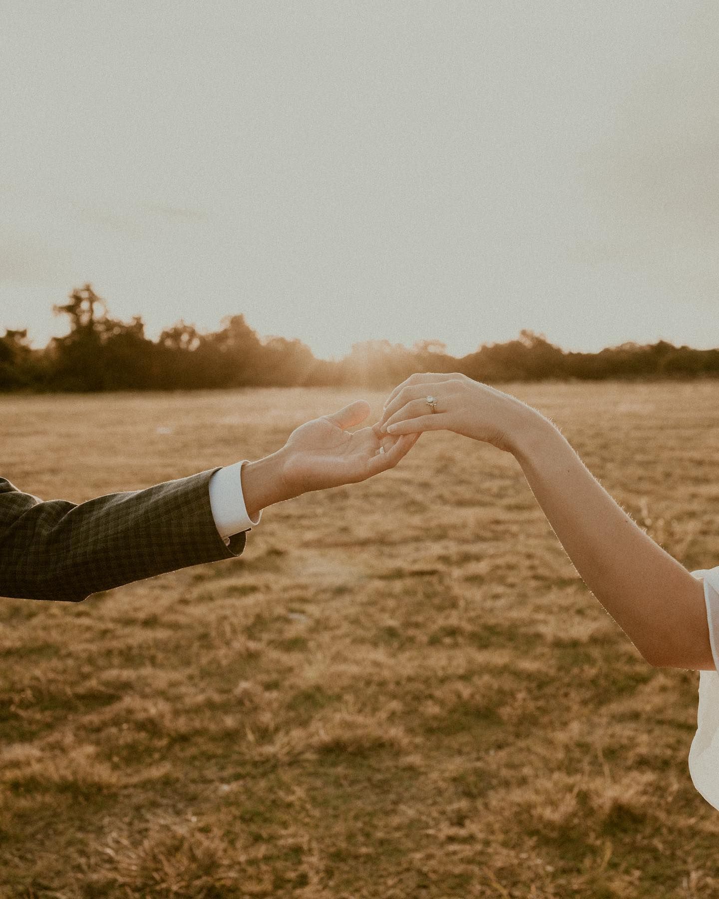 Intimate hands touching during golden hour in an open field.
