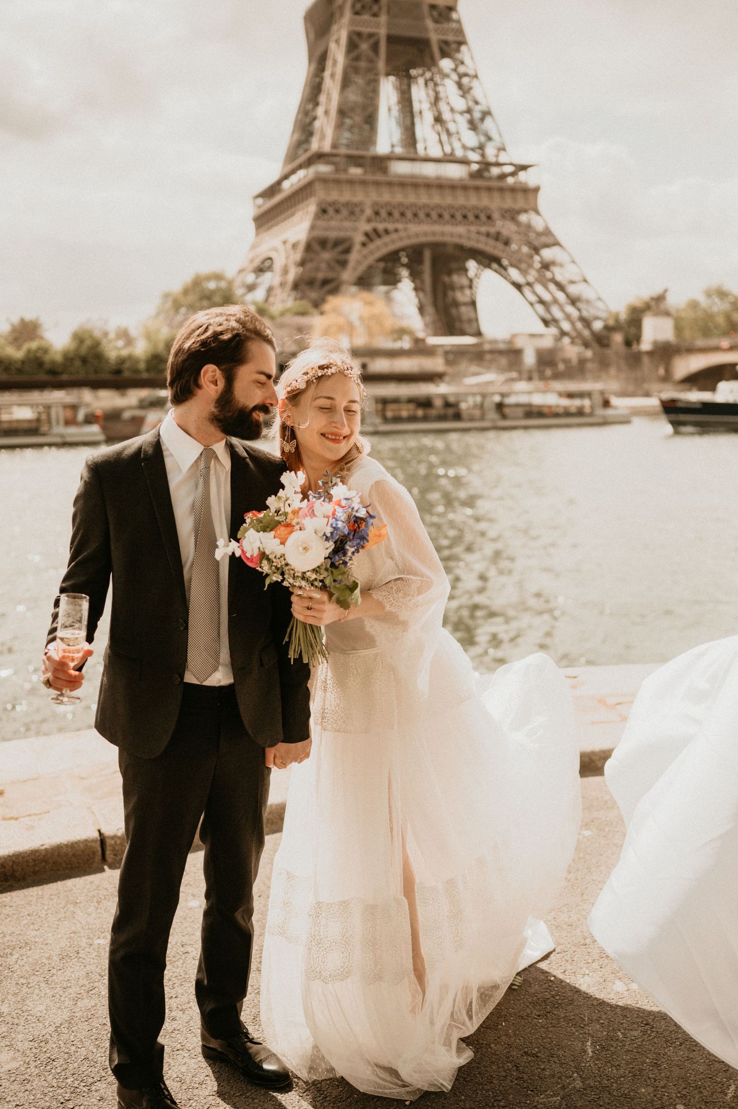 Happy bride and groom pose together with bouquet by the Seine River in Paris.