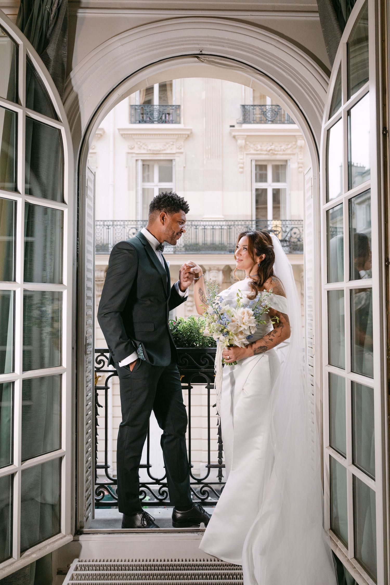 A romantic wedding couple stands in an elegant French doorway with ornate architecture and a beautiful city view.