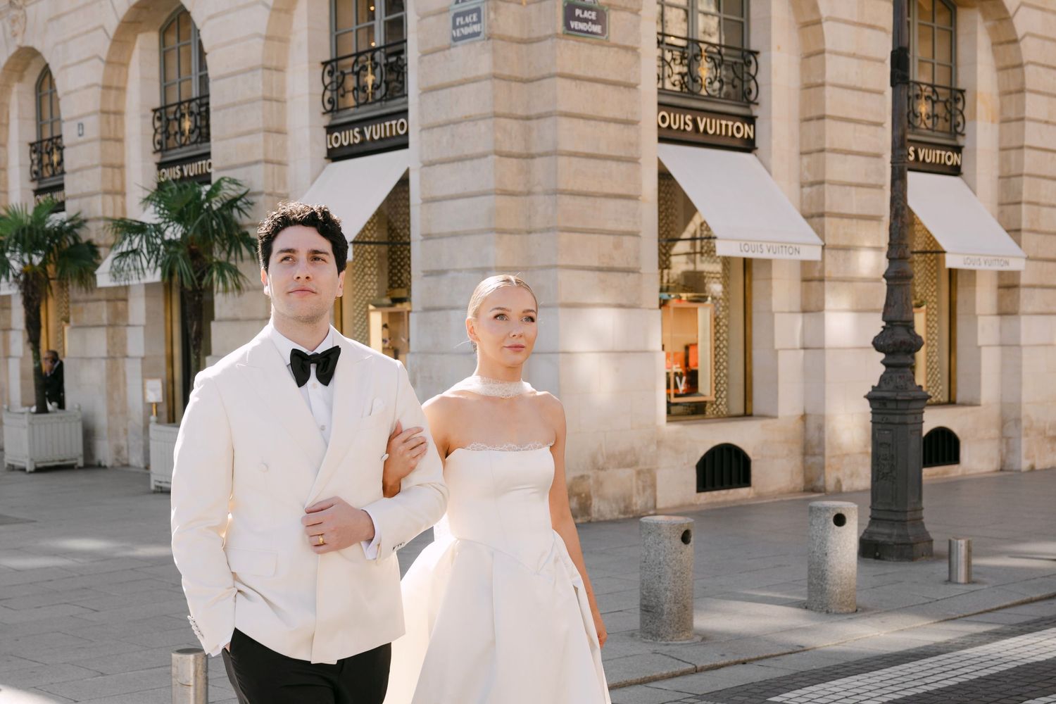 Elegant wedding couple poses in front of stone archways and columns at a grand European-style venue.