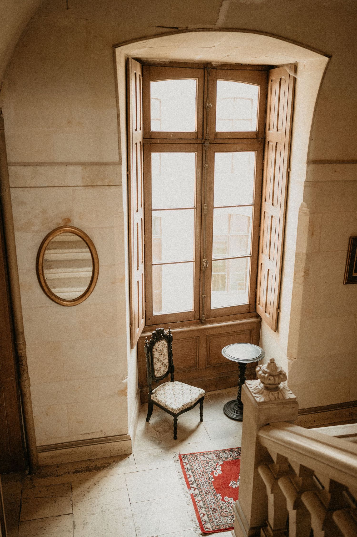 Elegant alcove with tall French windows, antique chair and round mirror.