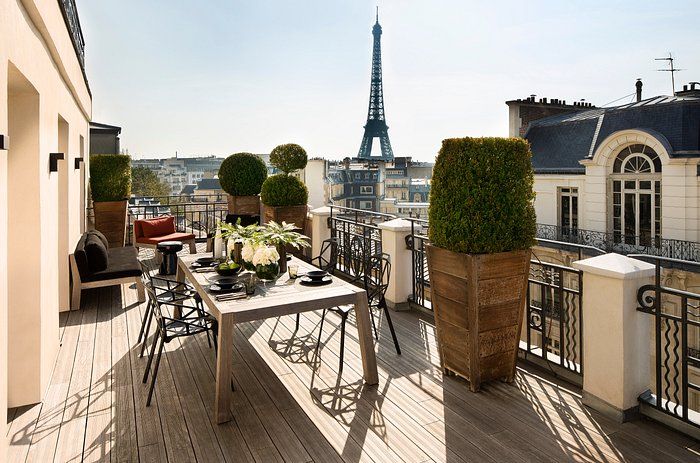 Sunny terrace with dining set and topiaries overlooking Paris rooftops with Eiffel Tower vista.