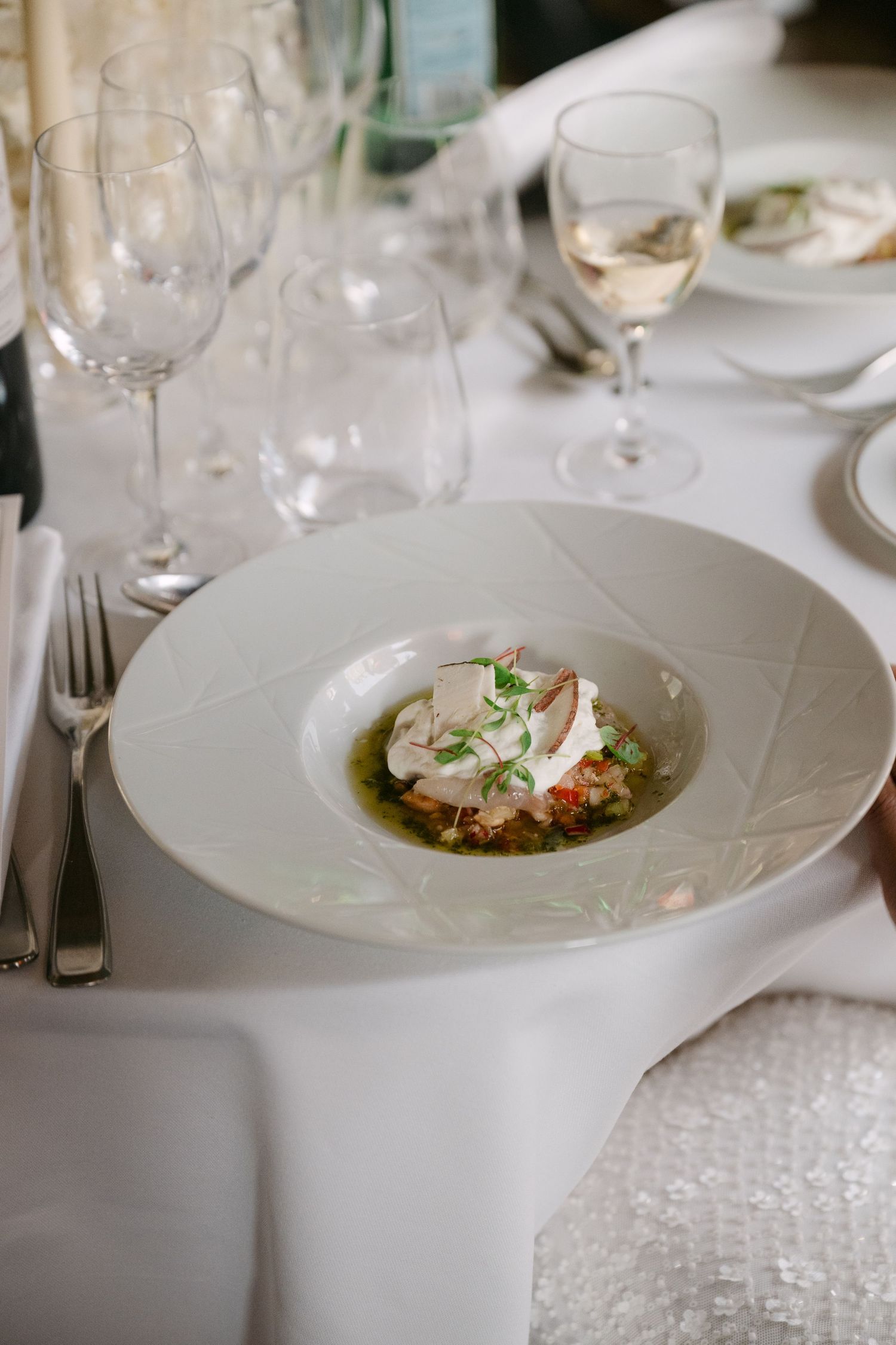 Elegant plated dishes at a fine dining restaurant with white tablecloths and wine glasses.
