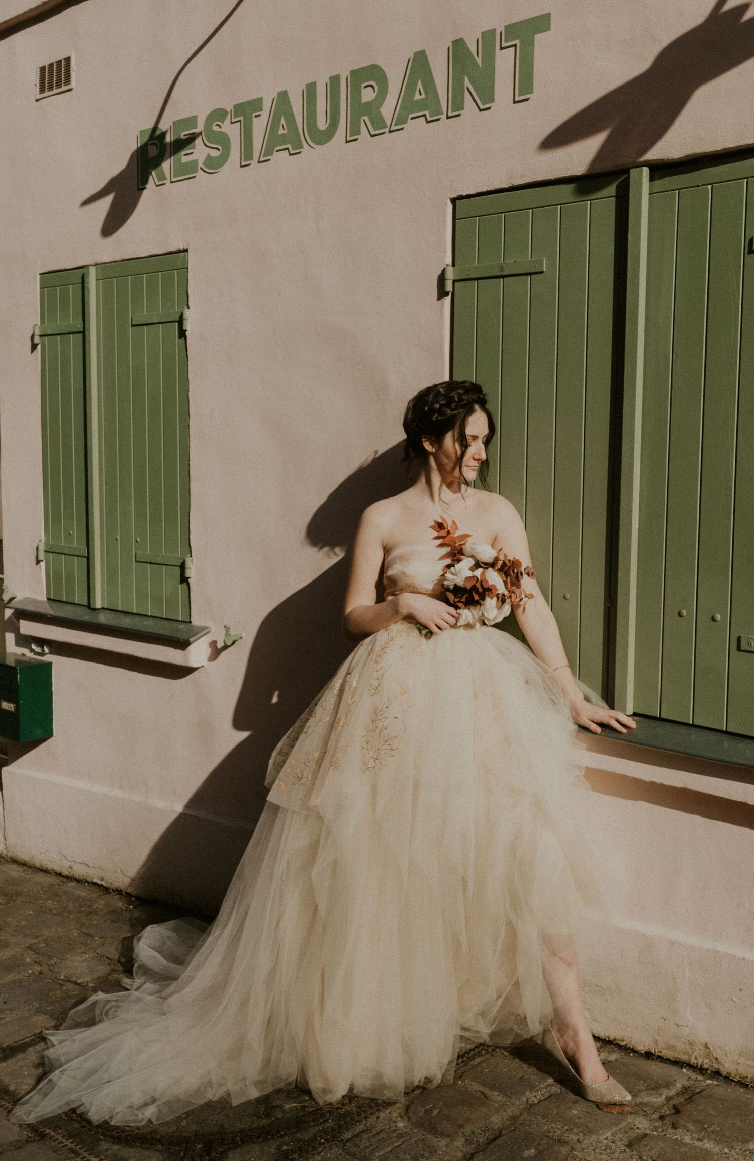 Ethereal bridal photo against a restaurant facade with green shutters and soft shadows.