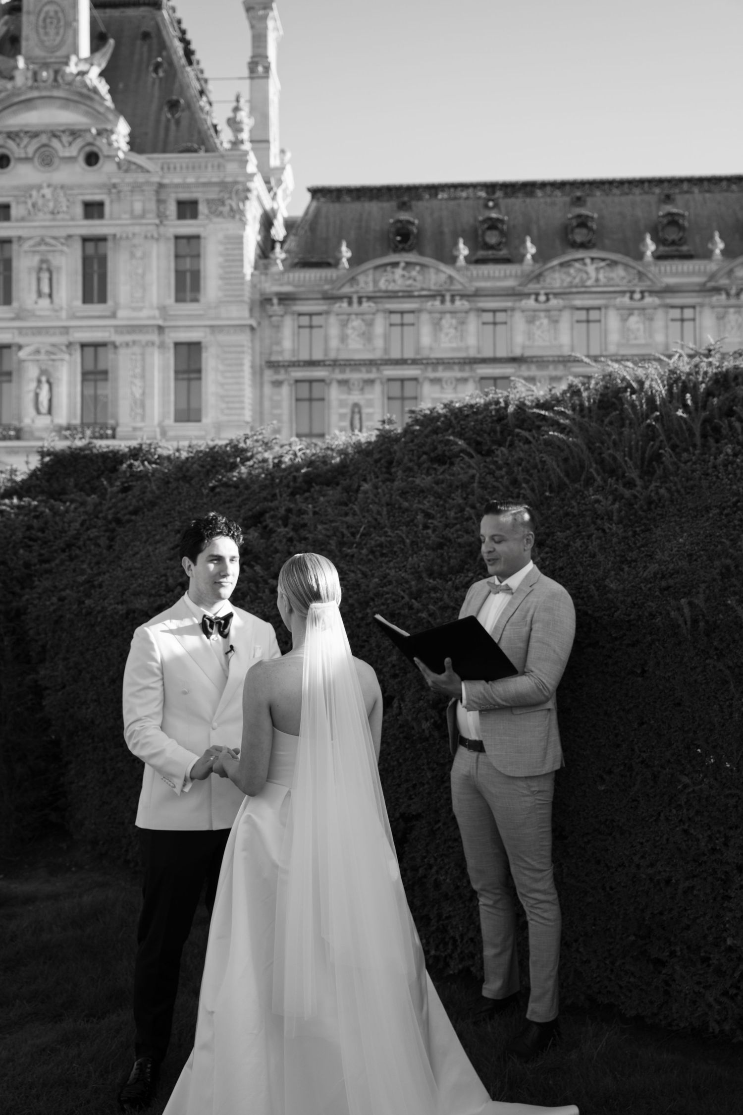 Black and white photo of a couple exchanging vows in front of the Louvre Museum in Paris.