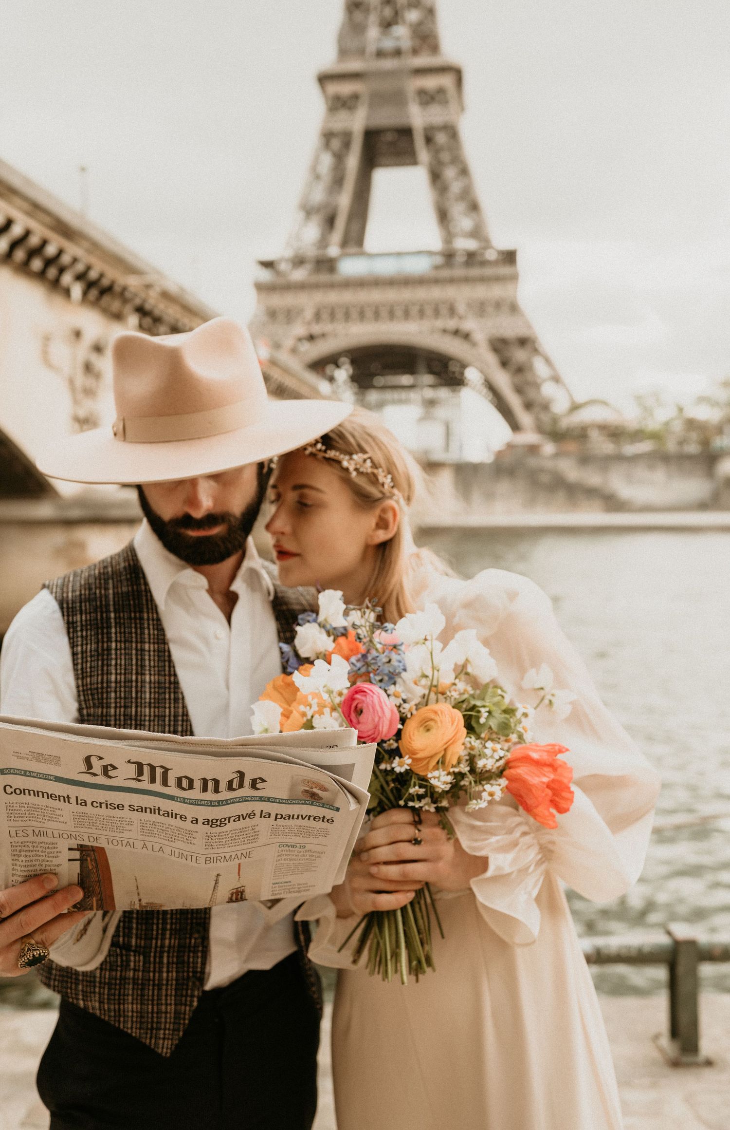 Dreamy Parisian photoshoot featuring vintage style couple with flowers and newspaper by Eiffel Tower.