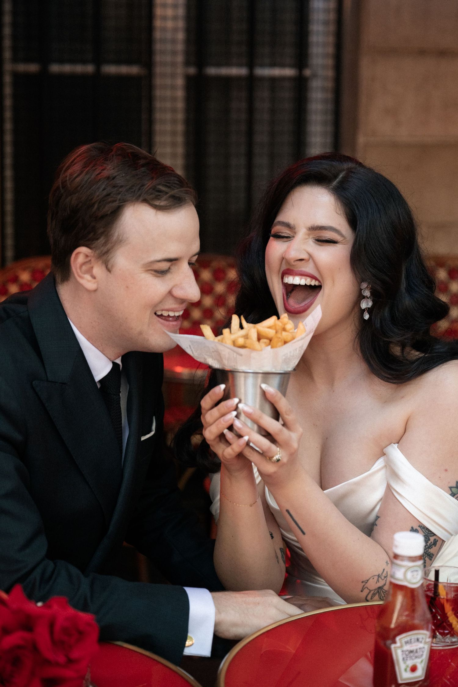 A couple sharing french fries and laughing together during their wedding reception.