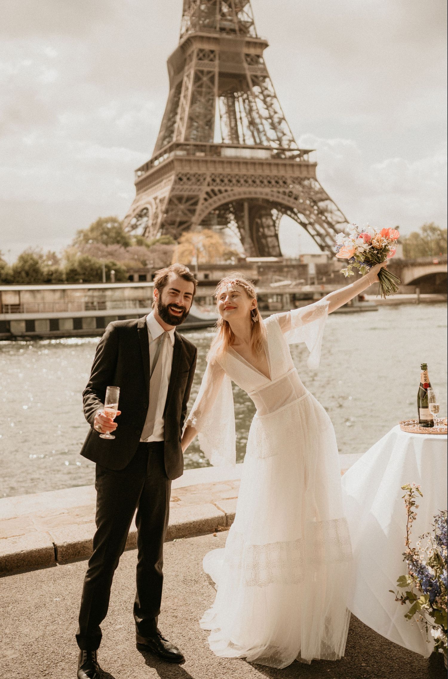 Newlyweds share a celebratory moment with drinks and flowers near the Eiffel Tower.