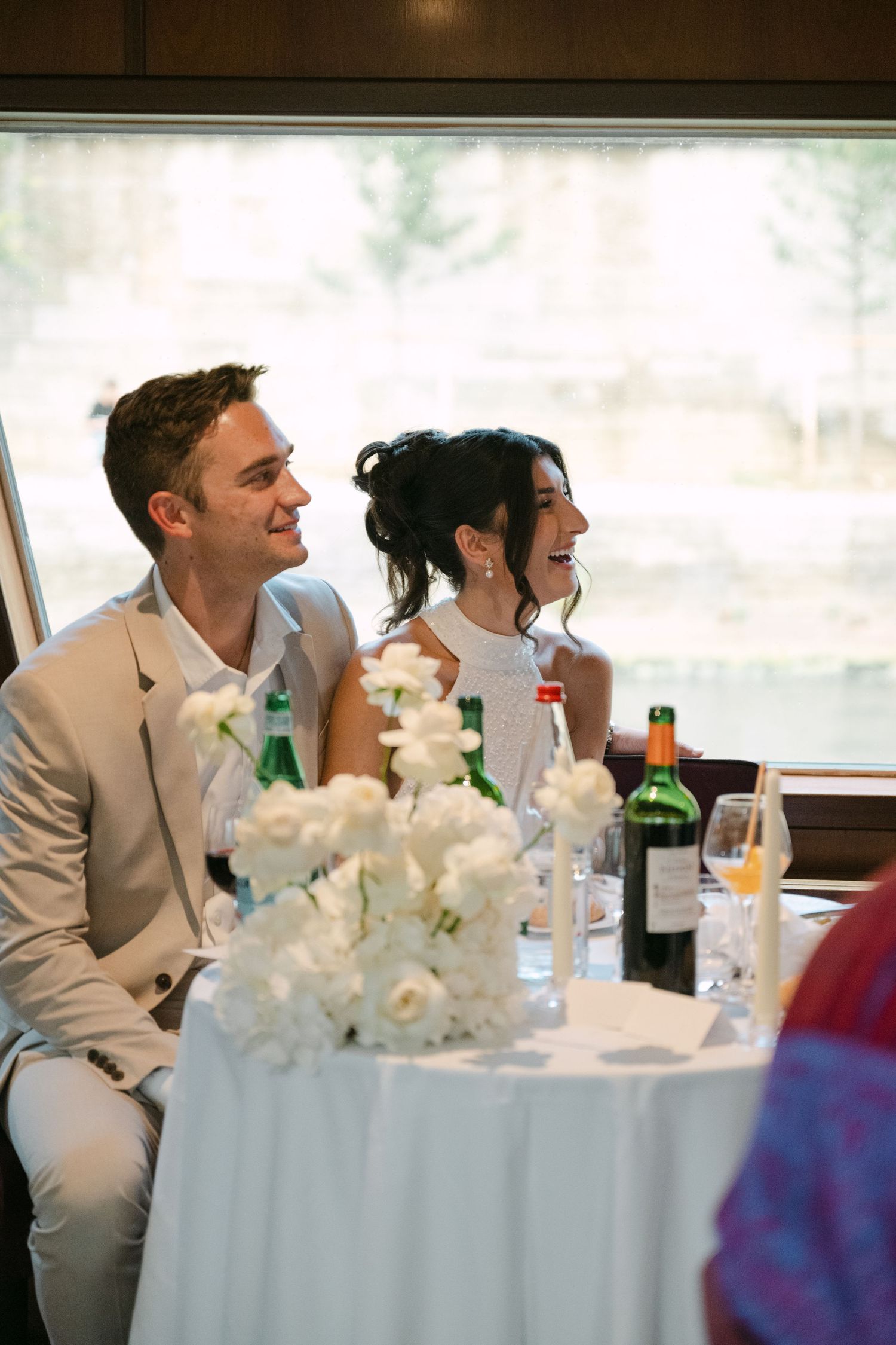A couple shares a joyful moment at their wedding reception table decorated with white floral centerpieces.