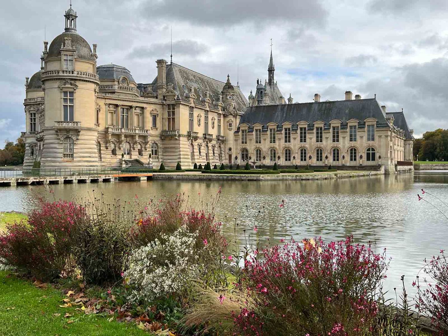 Majestic Chantilly Castle reflecting in the lake with colorful flowers in the foreground.