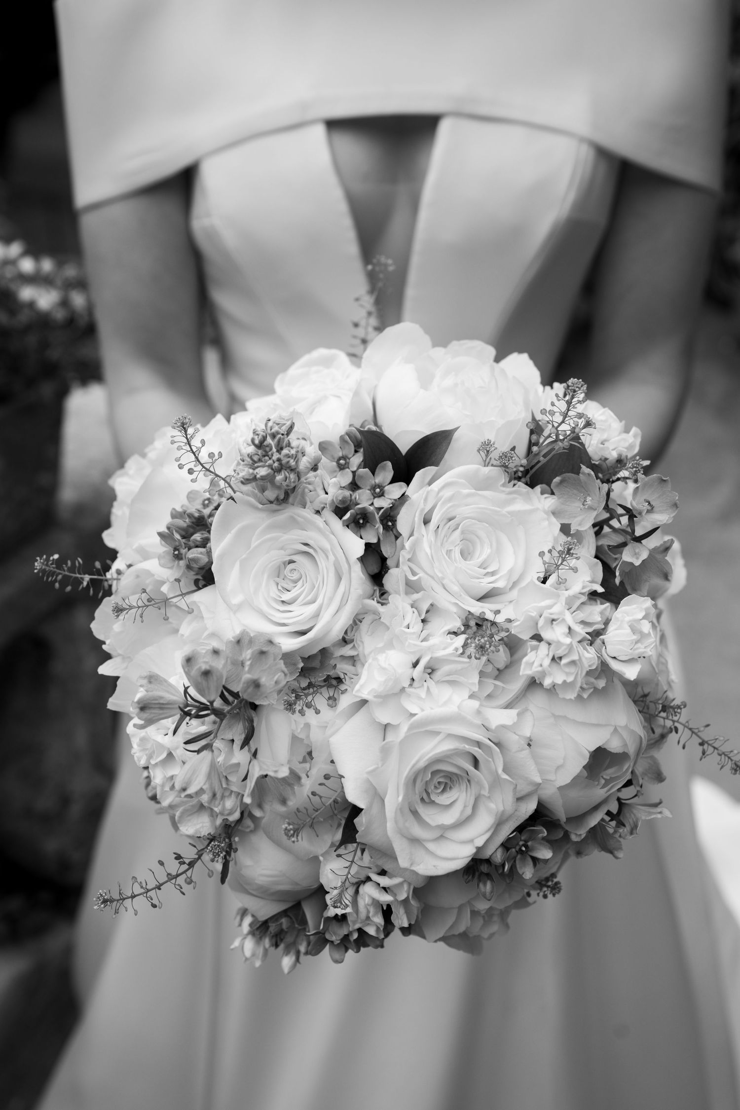 Black and white close-up of bride holding a lush rose bouquet in a strapless wedding gown.