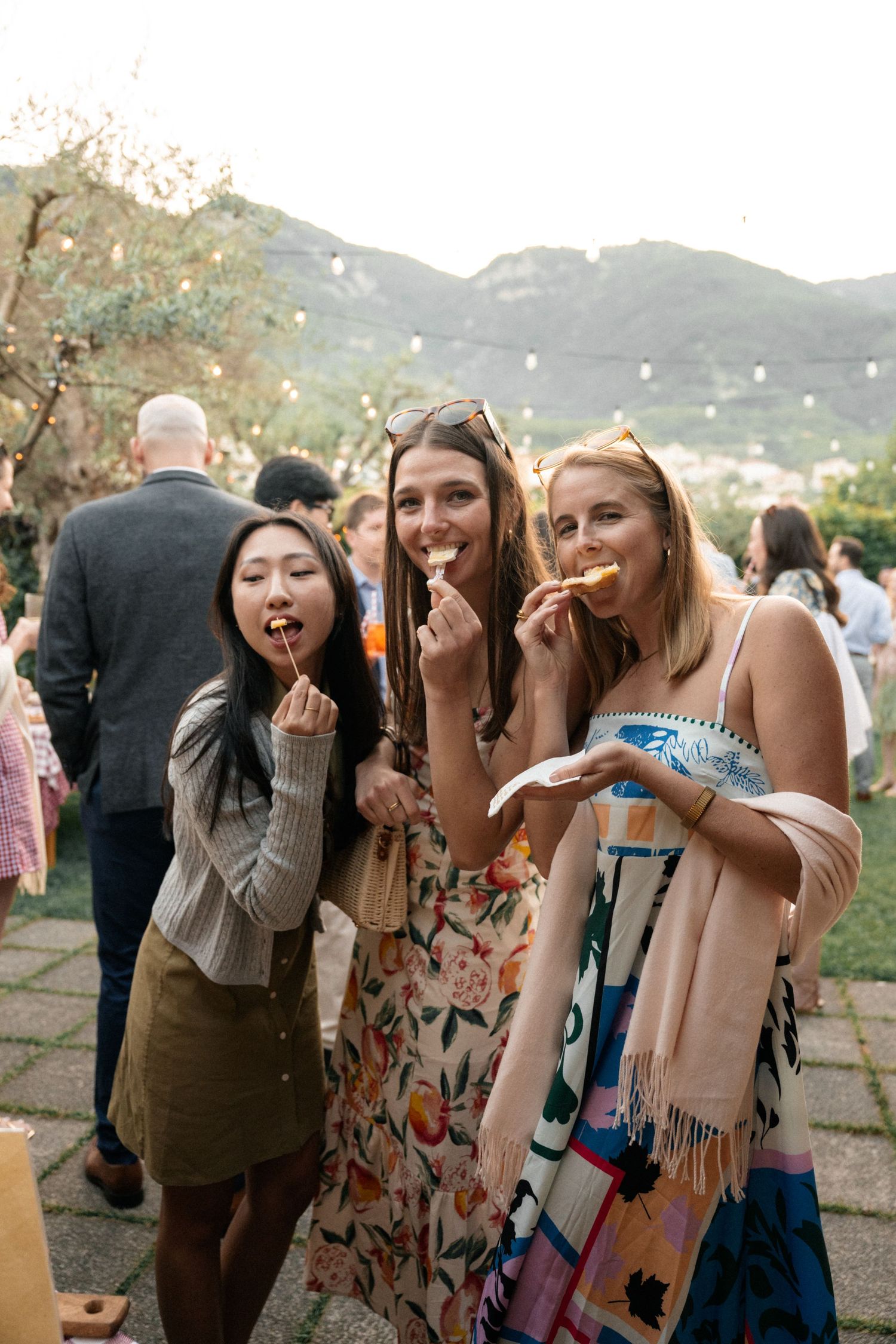 Three smiling wedding guests enjoy appetizers at an outdoor Italian hillside garden cocktail reception.