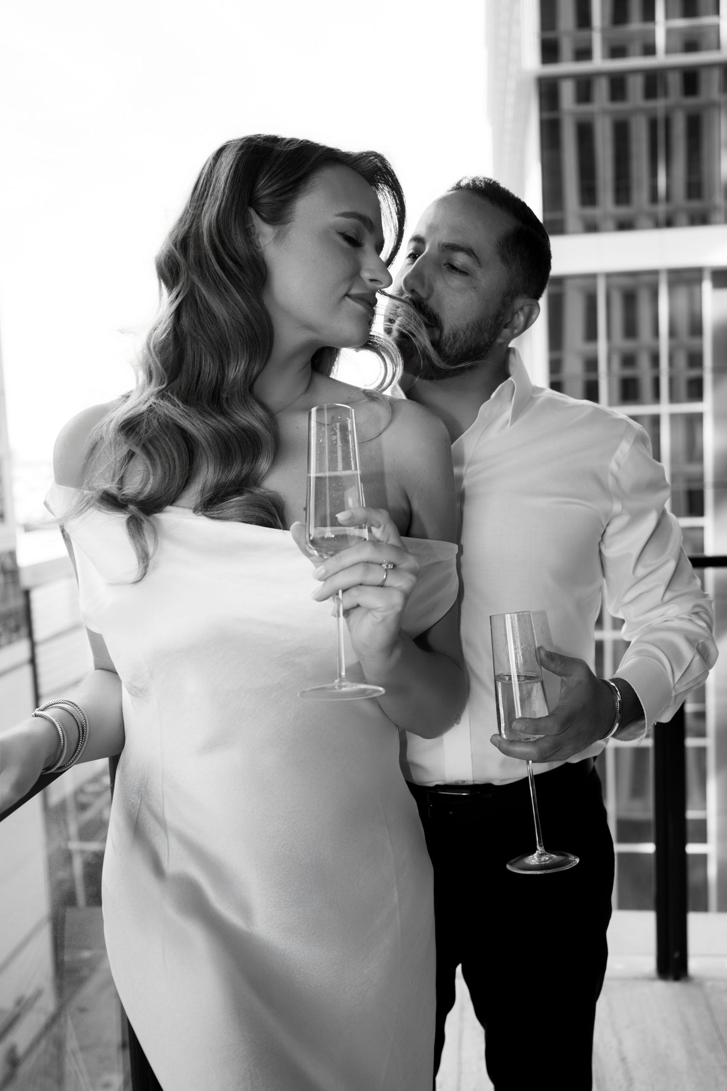 Black and white romantic photo of couple sharing champagne on an urban balcony.