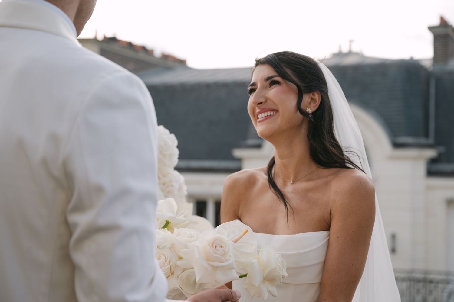 Beautiful bride in white strapless gown and veil smiles lovingly at groom during wedding ceremony.