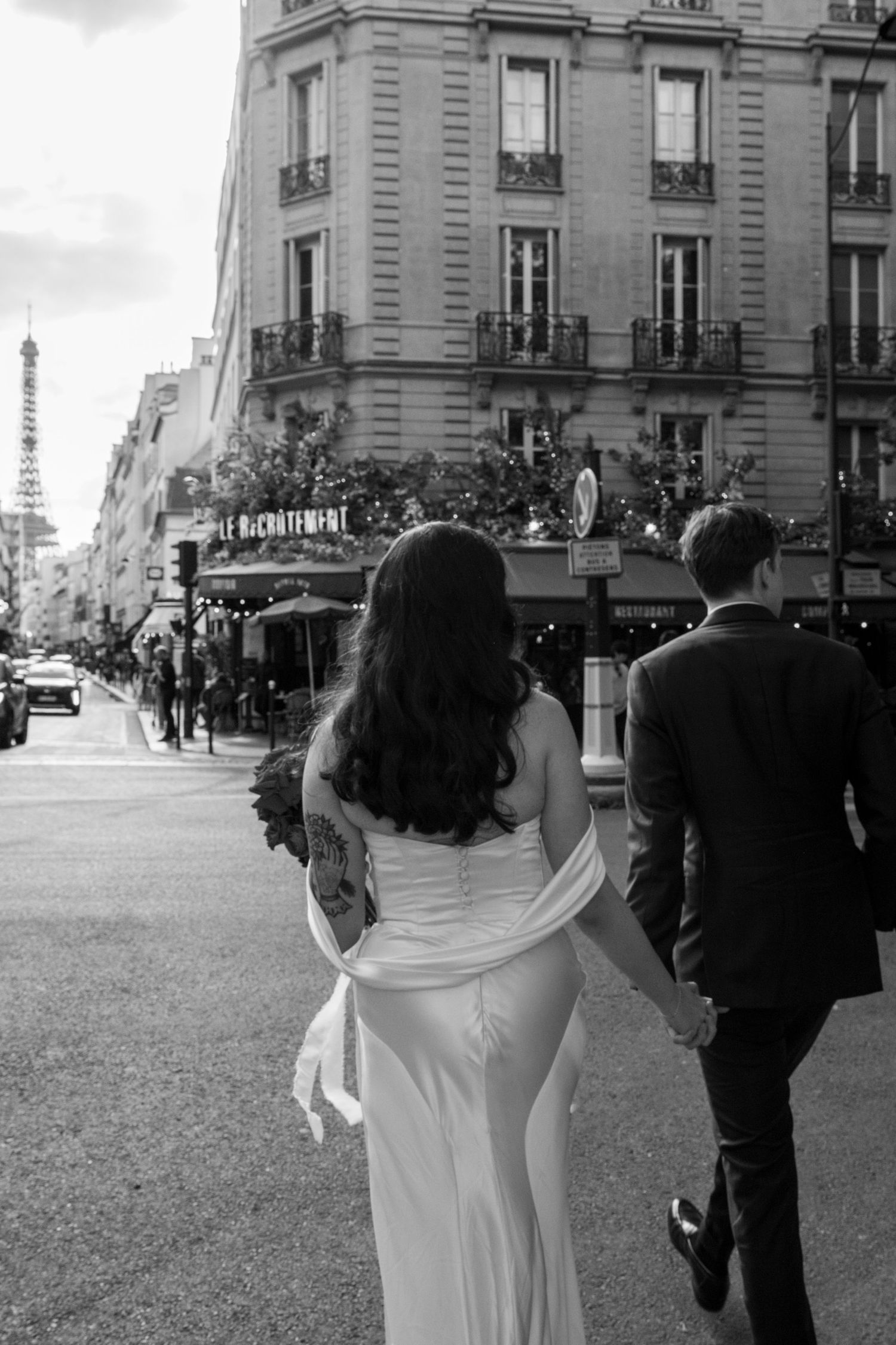 Black and white photo of bride and groom walking hand in hand on a Paris street.