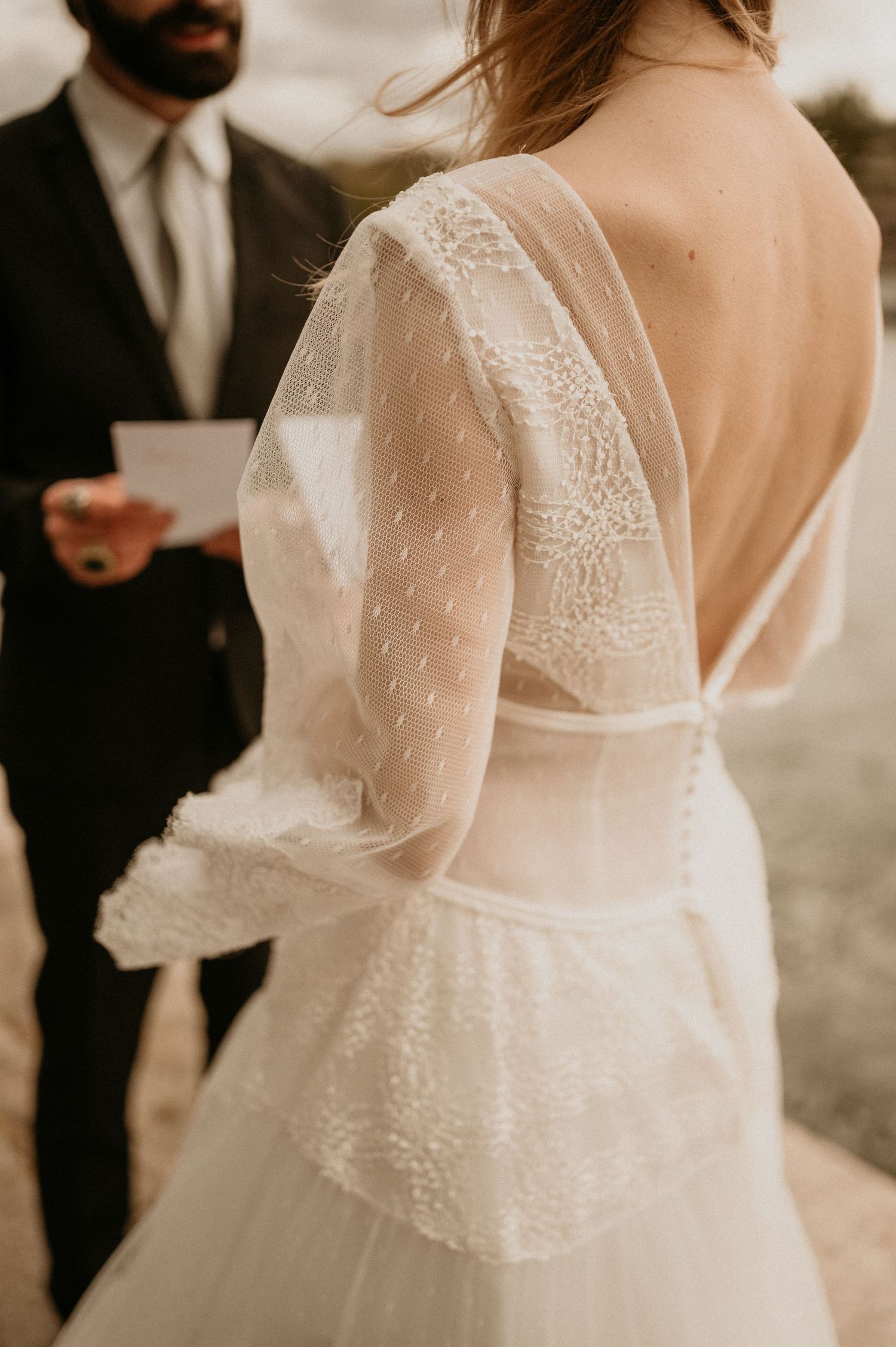 Detail shot of a bride's delicate lace wedding dress with sheer sleeves and open back.