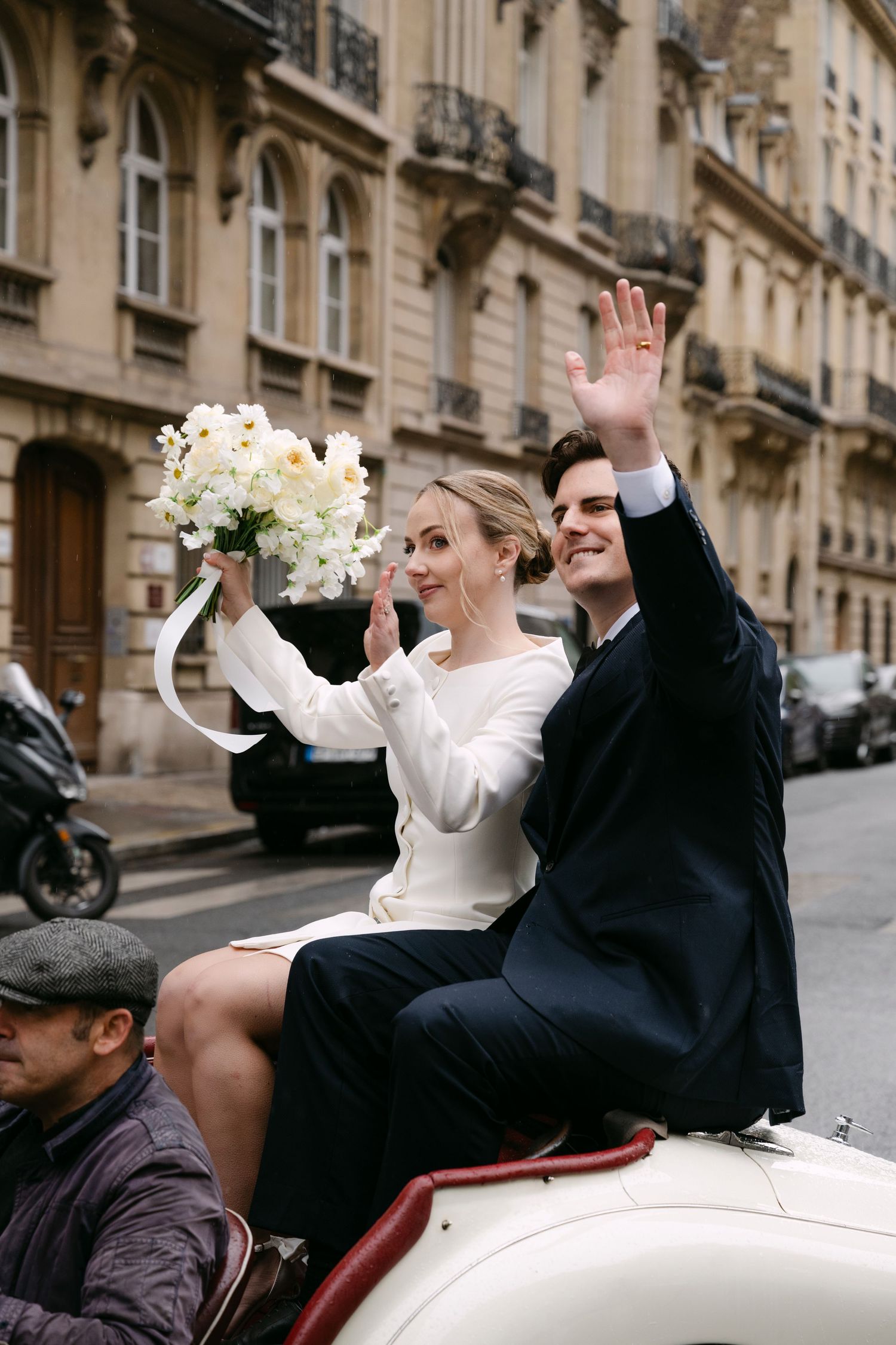 A celebratory moment captured in front of elegant Parisian buildings with a vintage automobile.