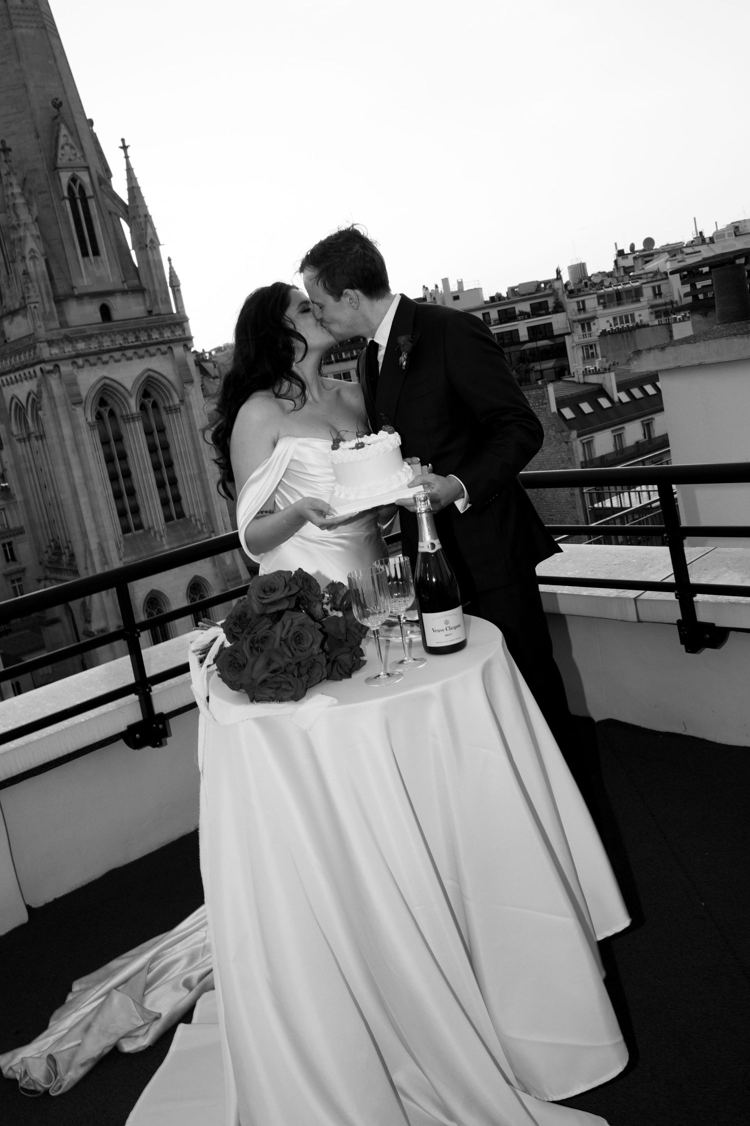 Romantic black and white photo of newlyweds sharing a moment at a table on a Parisian rooftop.