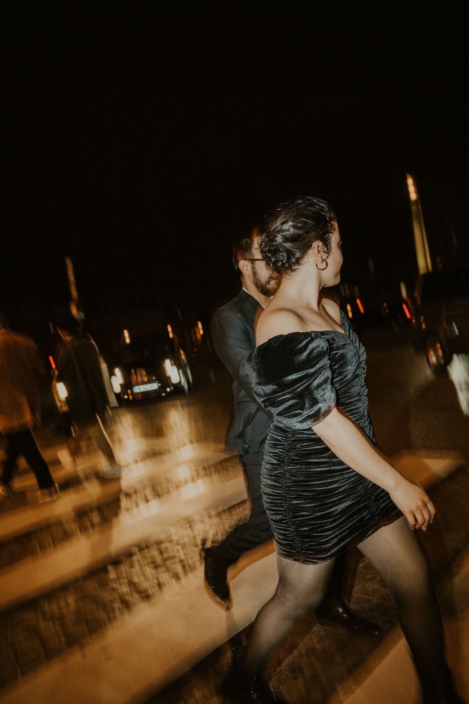 Person in black dress dancing under city lights at night.