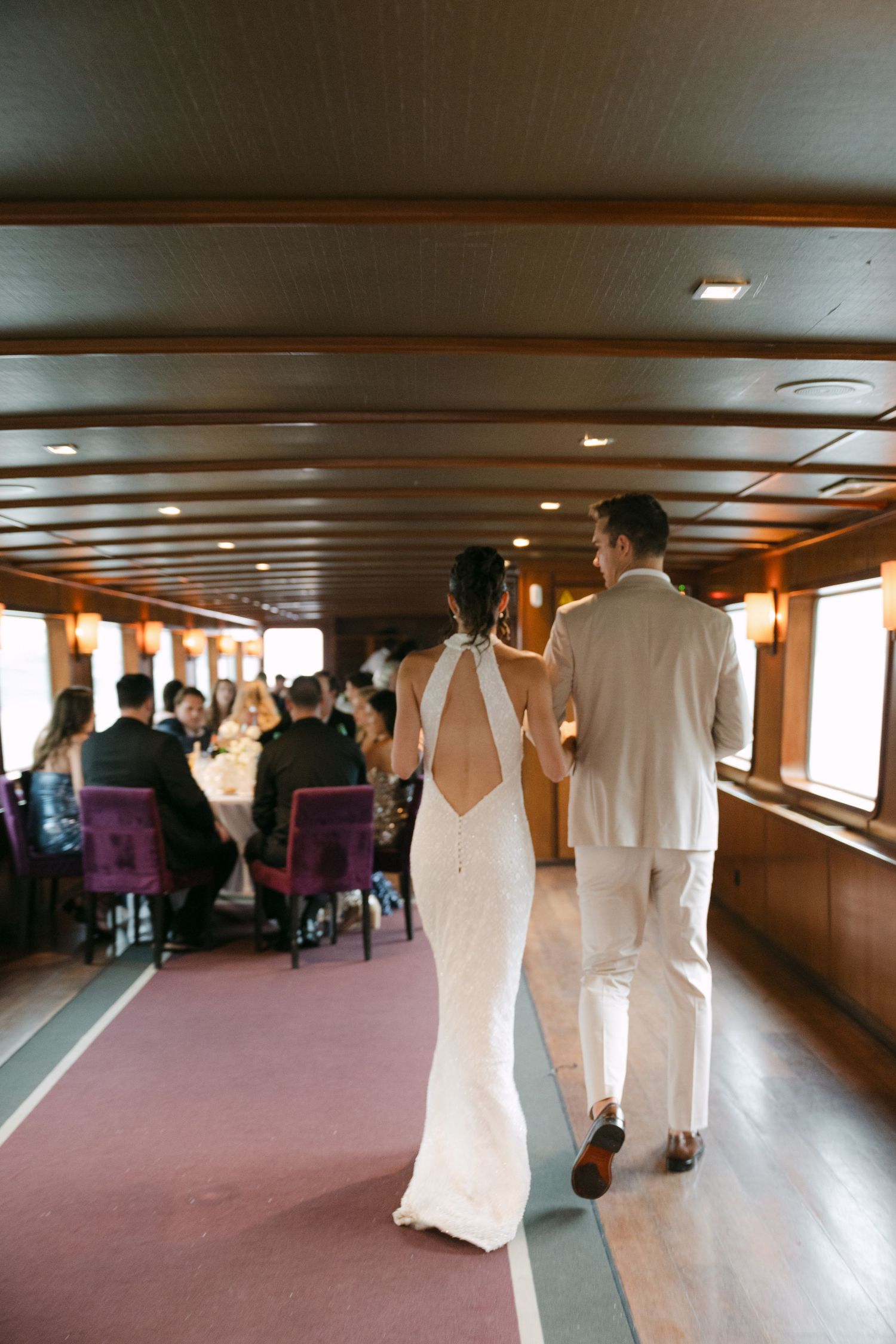 People gather in an elegant boat interior with wood paneling and purple seating during what appears to be an event.