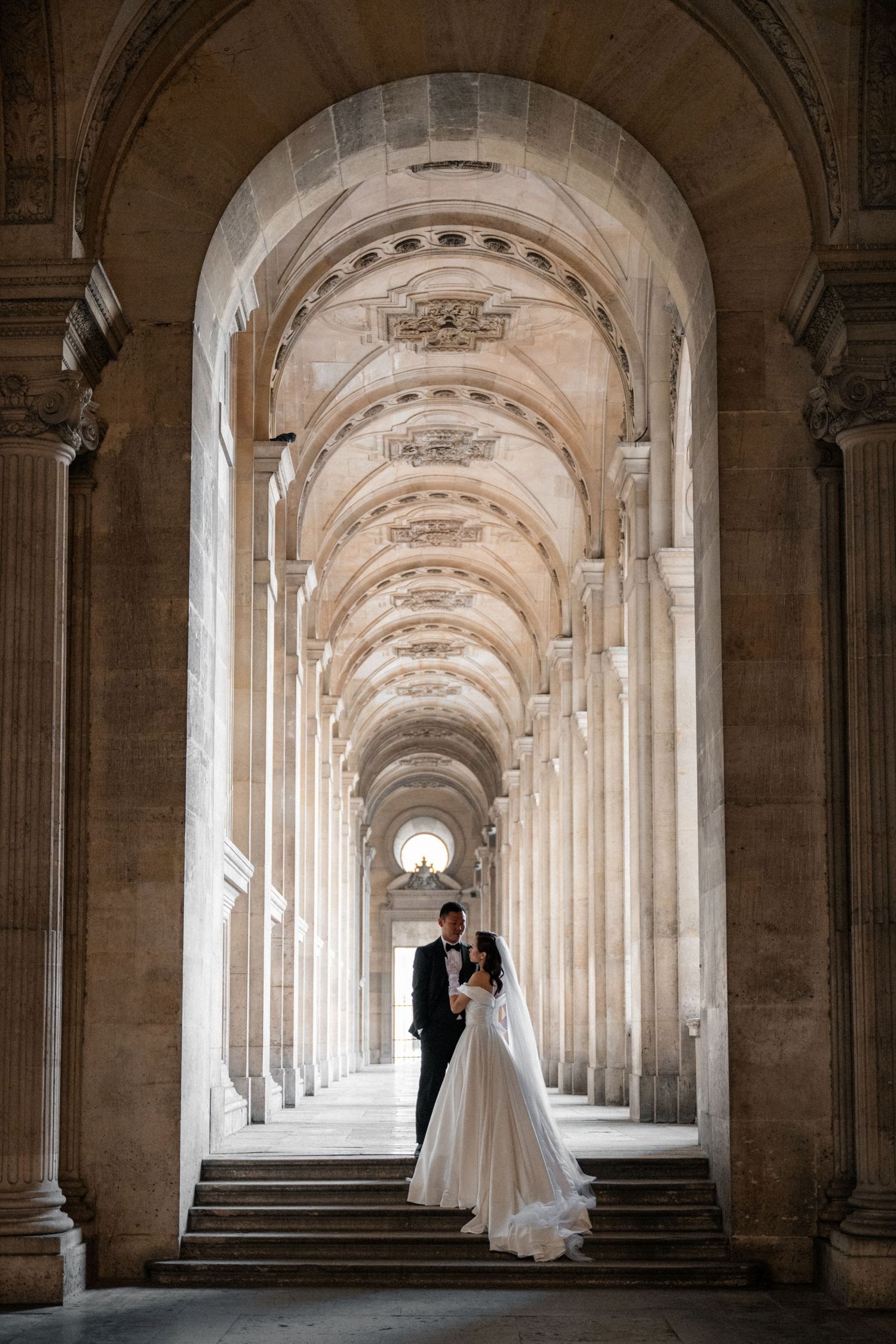 Wedding couple poses in front of the iconic Louvre Pyramid at sunset in Paris.