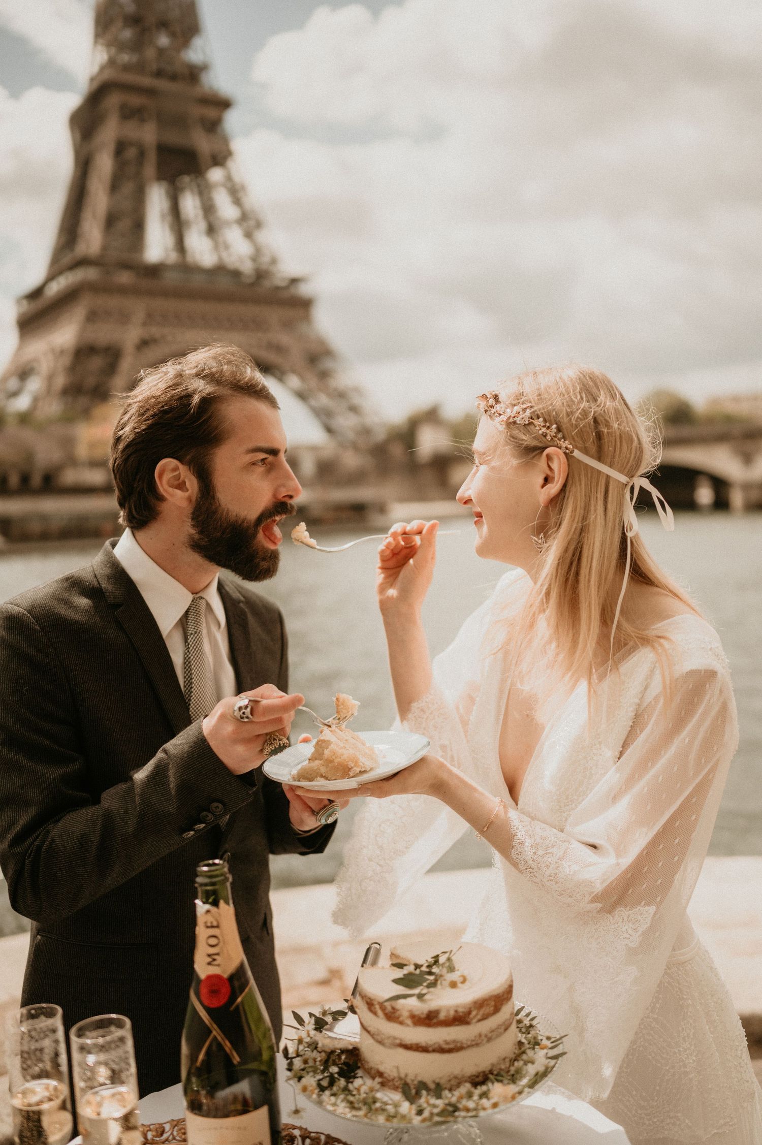 A candid moment of newlyweds enjoying wedding cake with Paris' iconic tower in the background.