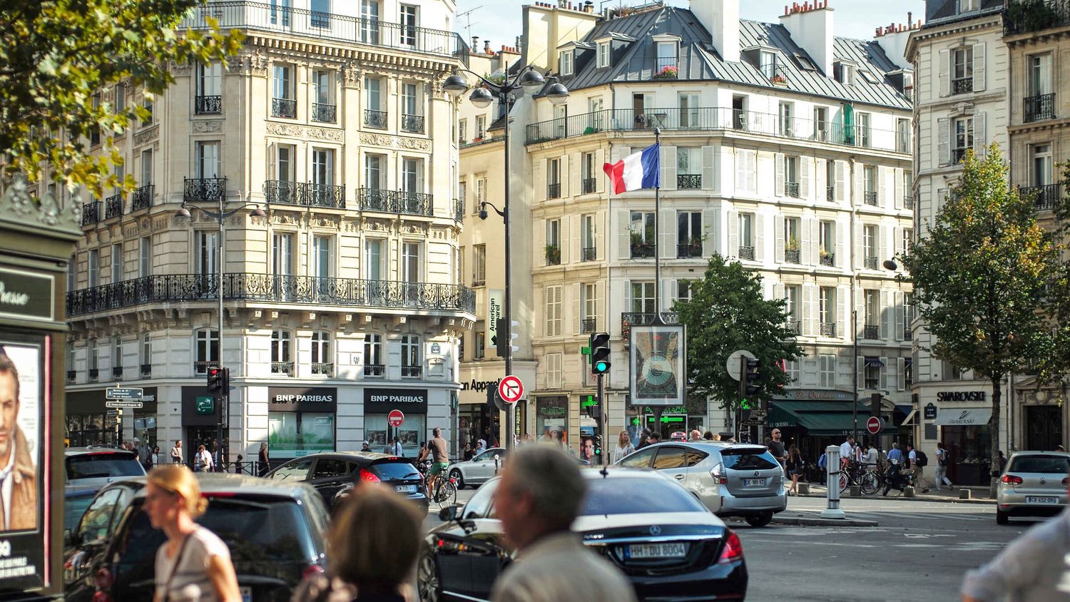 Classic Parisian intersection with historic Haussmann buildings and French flags on a sunny day.