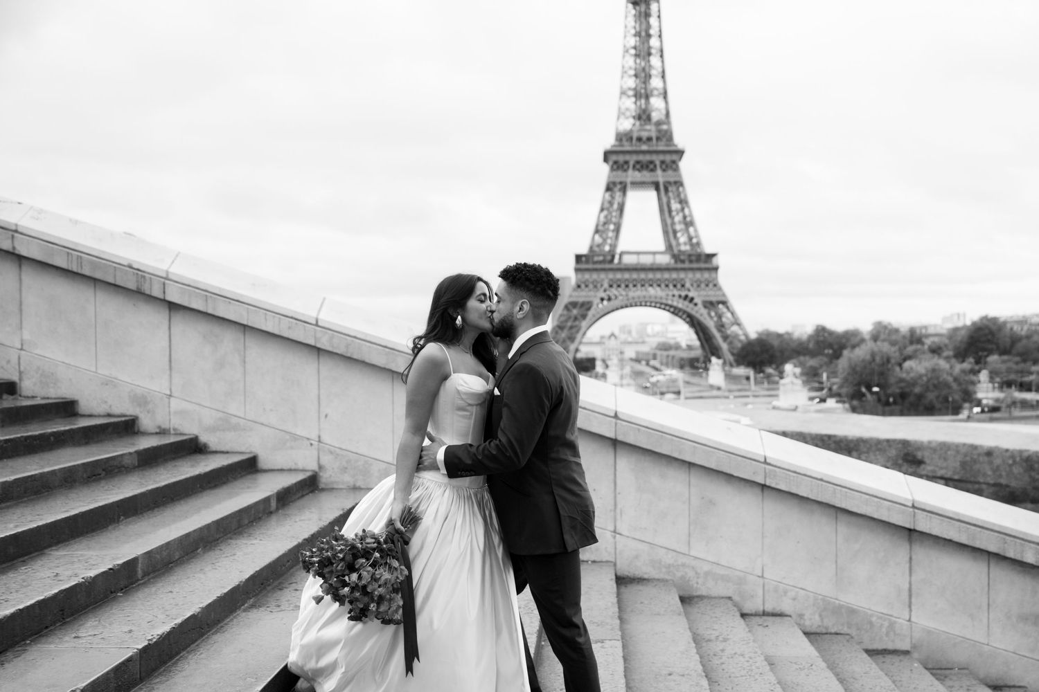 Couple shares a romantic kiss near the Eiffel Tower in this black and white Paris wedding photo.